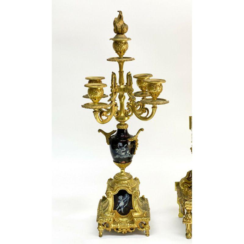 3 piece gilt bronze clock garniture, late 19th/early 20th century.

3 Piece Gilt Bronze Clock Garniture. Enameled copper plaques with hand painted white cherubs mounted to the bases and joints, the bronze accented by gilt leaves and foliate