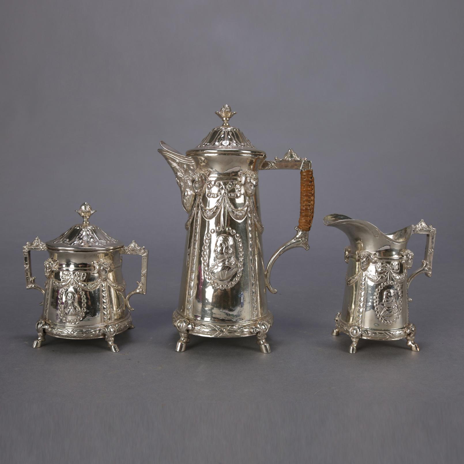 Three piece German .800 silver petite tea set by Georg Roth Hanau features repousse rams heads, garland drape with bows, and bead framed reserves with cameos; each raised on hoof feet; includes tea pot, covered sugar and creamer, hallmarks on base