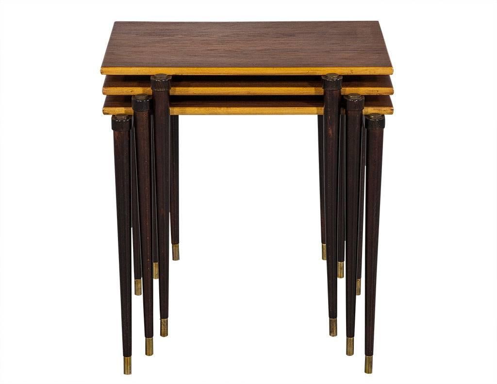 This midcentury style set of nesting tables is uber trendy. Each is composed of a walnut tabletop with ebonized legs adorned with brass caps. An interesting set perfect for any home.