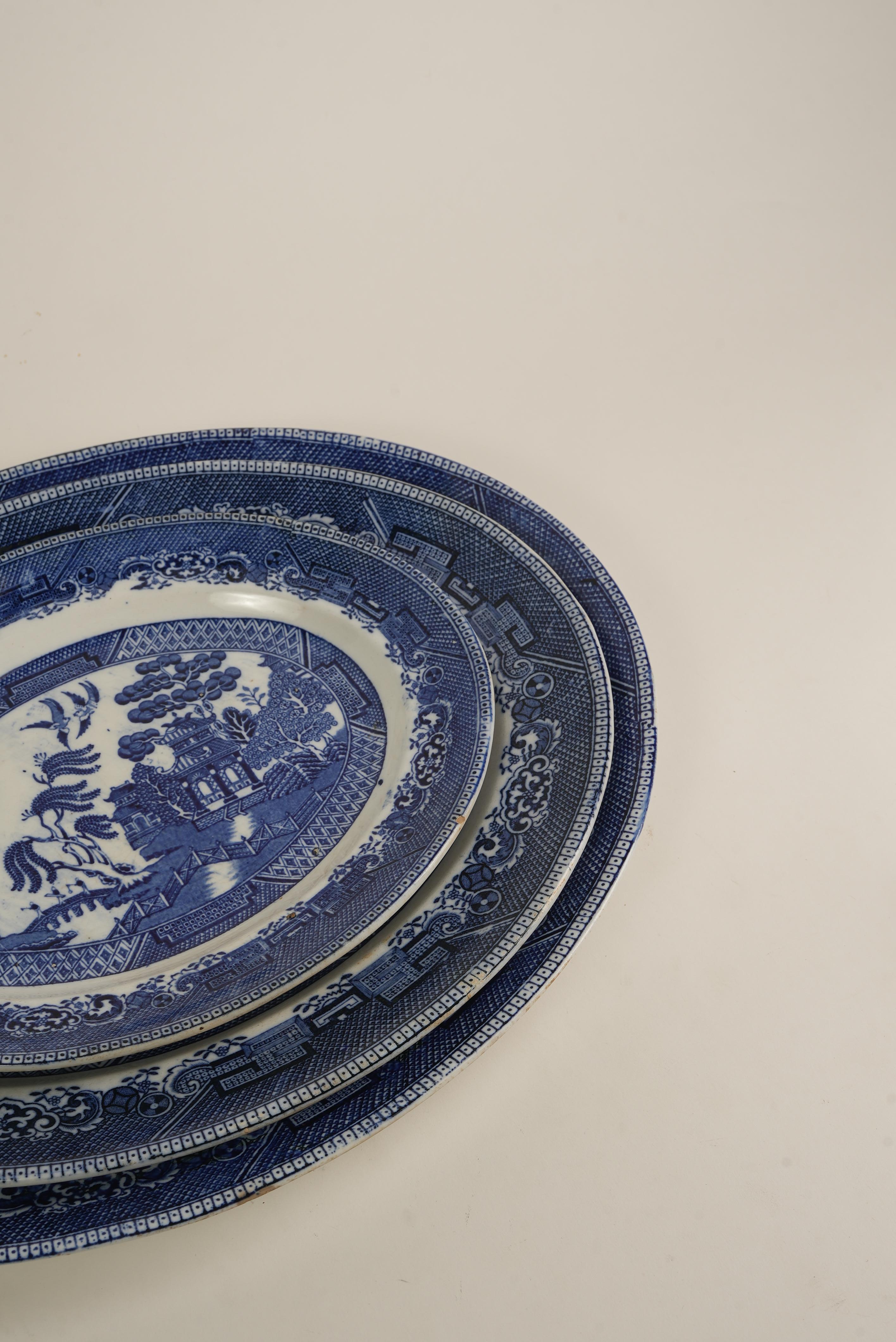 This vintage oval serving platter is a striking example of the iconic Blue Willow pattern, a design that has captivated collectors for over two centuries. What sets this piece apart is its finely detailed transferware scene — featuring elegant