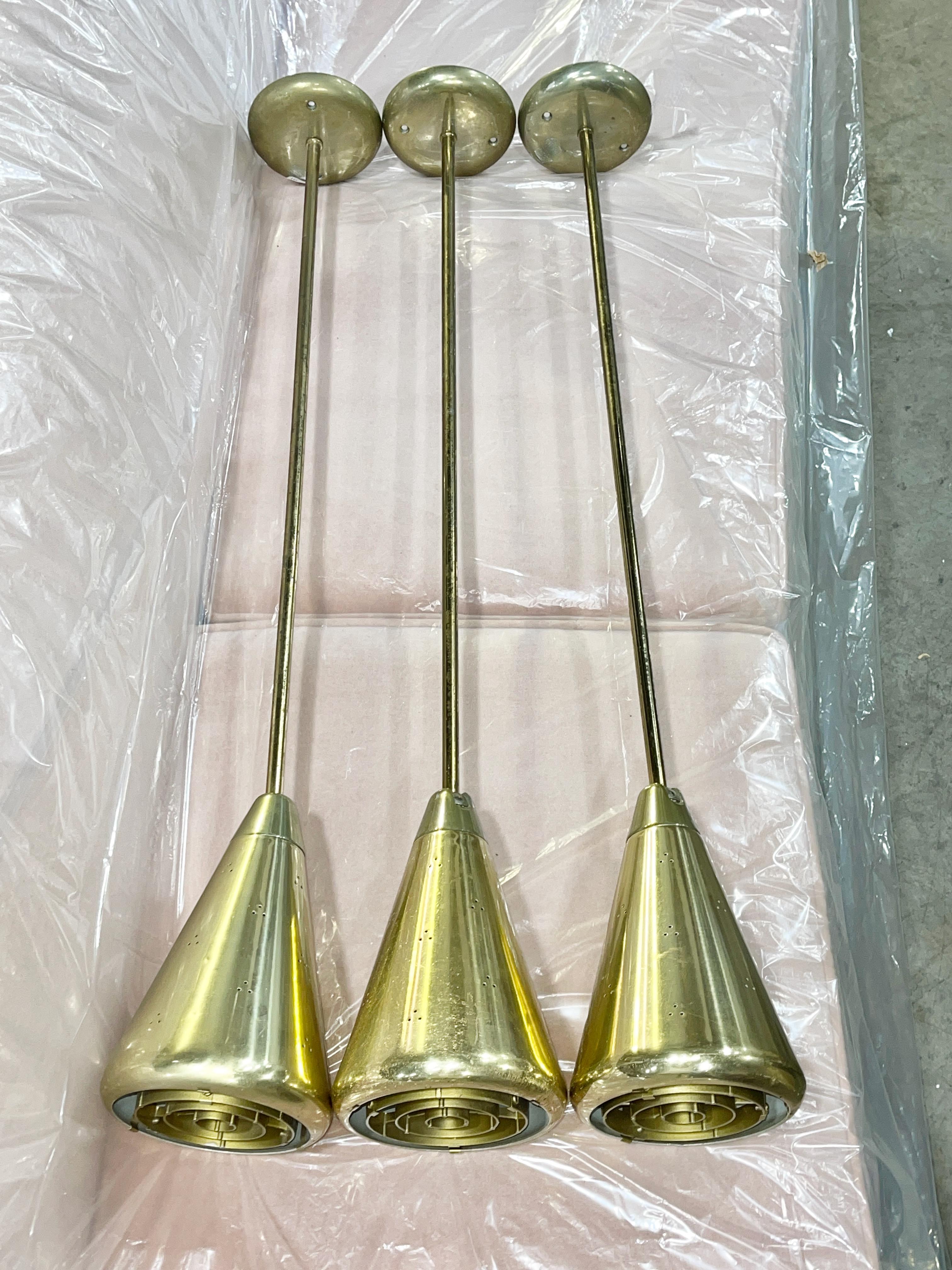 Juego de 3 lámparas colgantes cónicas articuladas de aluminio en tono latón. Estas lámparas de techo colgantes tienen pantallas cónicas redondeadas en forma de embudo, perforadas en un patrón triangular repetitivo por todas partes, con ángulos de