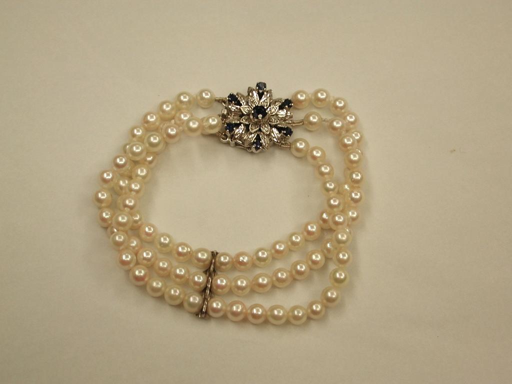 bracelet de perles de culture à 3 rangs avec fermoir en or blanc 9ct serti de saphirs, 1984
Perles de culture bien assorties et perles en forme de fleur en 9ct  bouton pression en or serti de saphirs et de diamants.
Fabriqué à Londres.