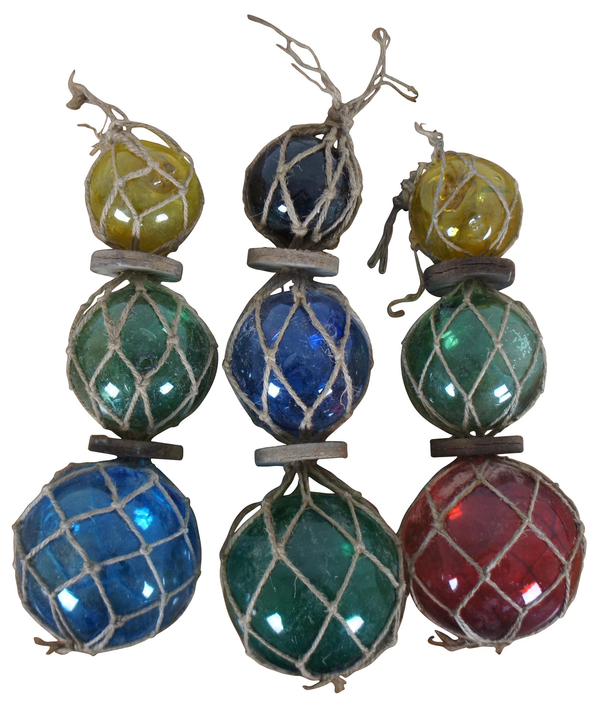 Set of three vintage Japanese hand blown glass fishing buoy floats, featuring red, green, blue, yellow and dark amber graduated glass orbs, divided by cardboard discs and suspended in jute netting.
