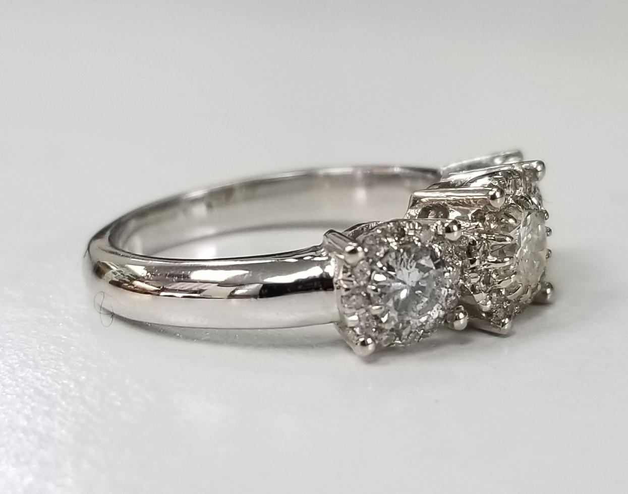 3 stone 14 karat diamond halo ring, containing 3 brilliant cut diamonds of fine quality weighing .76pts. and 38 round full cut diamonds of very fine quality weighing .38pts. This ring is a size 6 but we will size to fit for free.