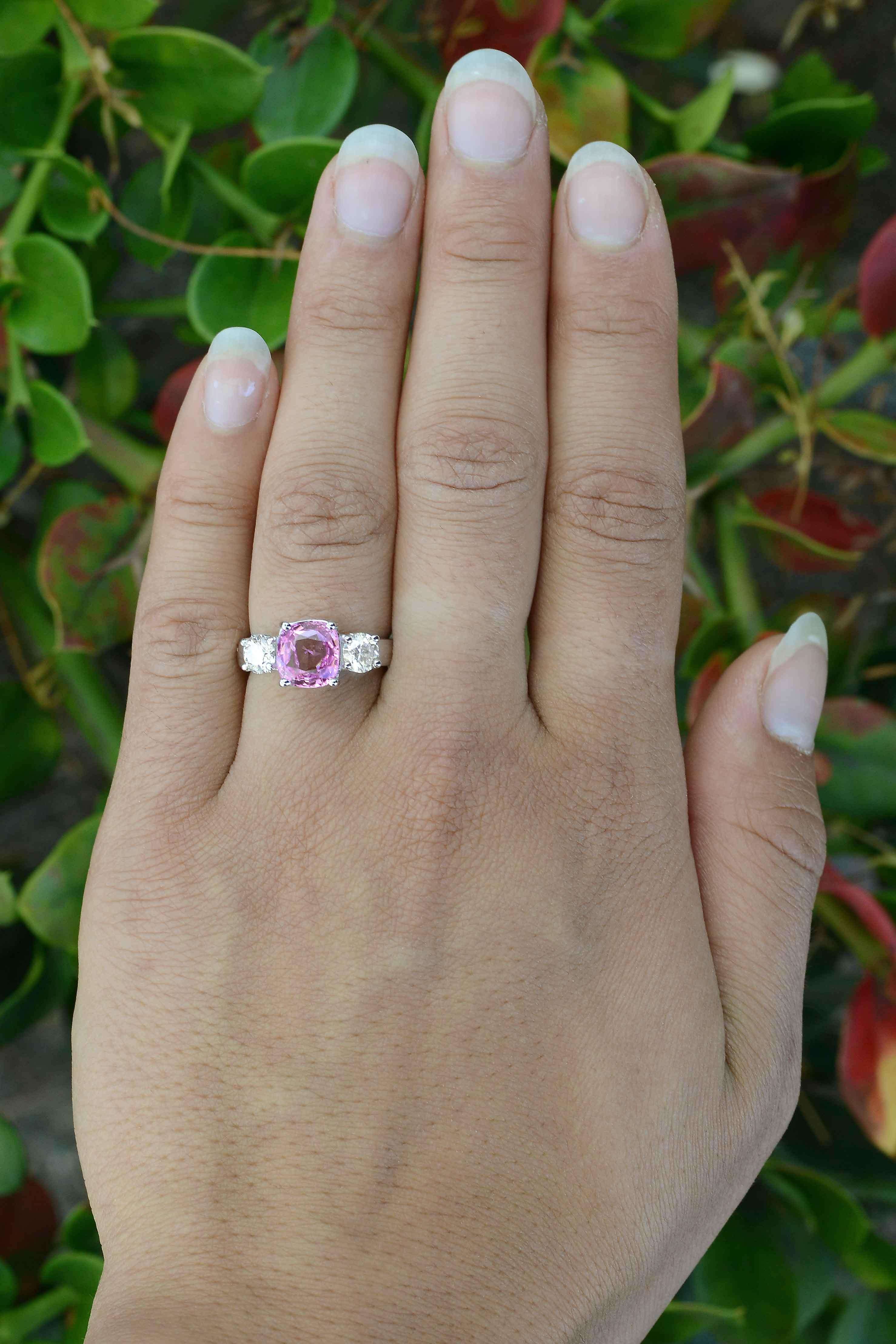 Taking center stage of this pink sapphire engagement ring is a 2.72 carat antique chunk of a tantalizing purplish pink color. GIA certified as natural, set in a trinity design, a timeless classic made with a reclaimed vintage gemstone and flanked by