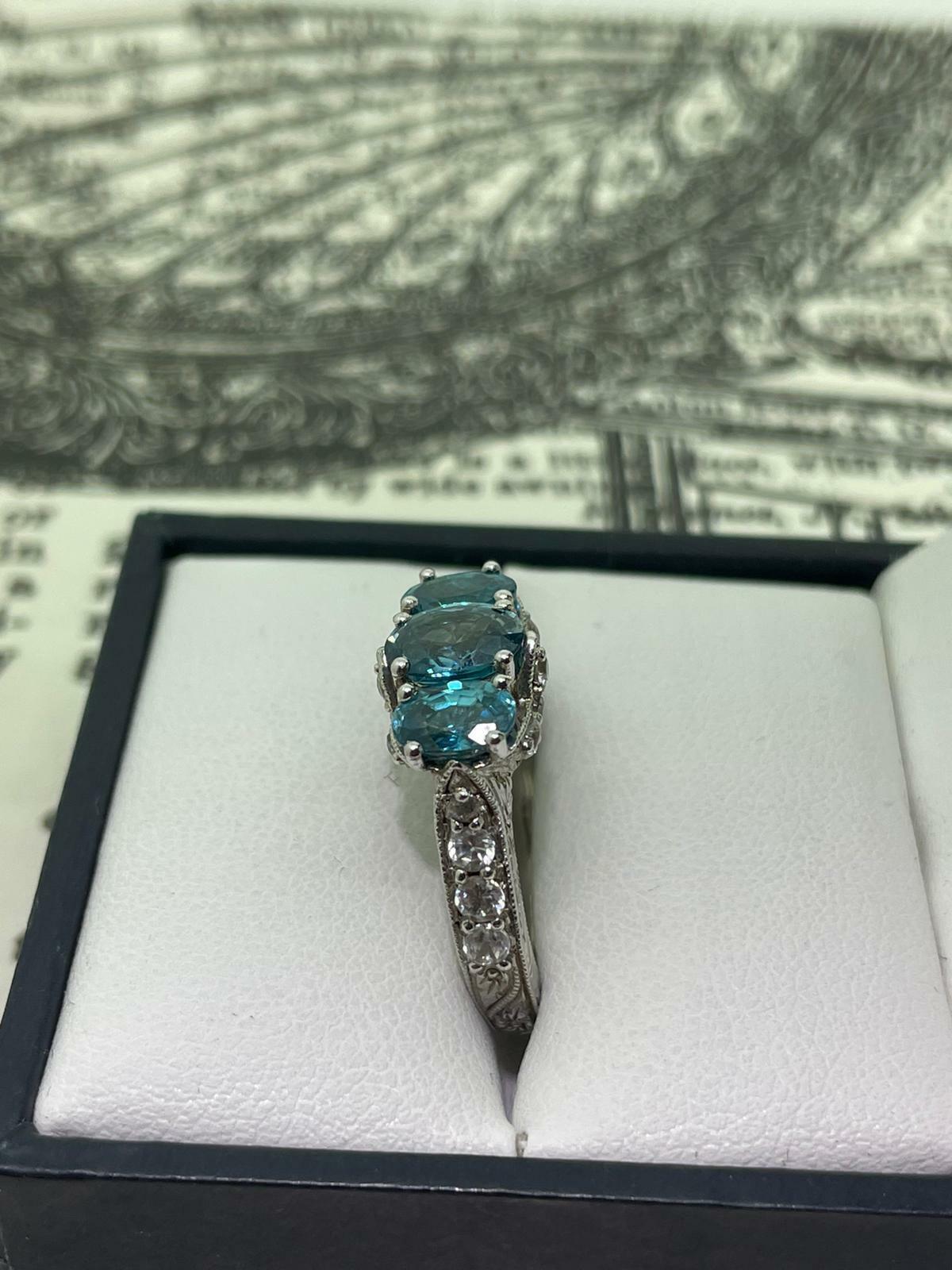 Meticulously Crafted in 925 Sterling Silver, 
this vintage ring is centering 
3 Oval Blue Topazes 
of 2.50ct in total approx. 
of stunning vivid blue colour, 

Set within gorgeous gallery, engraved in foliate motif 
decorated with finest quality
