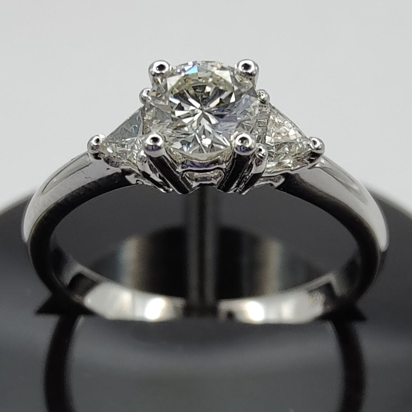 This three-stone diamond engagement ring is the epitome of timeless elegance and sophistication. The ring is made of 18k white gold, a material that is highly prized for its durability and shine. The white gold setting serves as the perfect backdrop