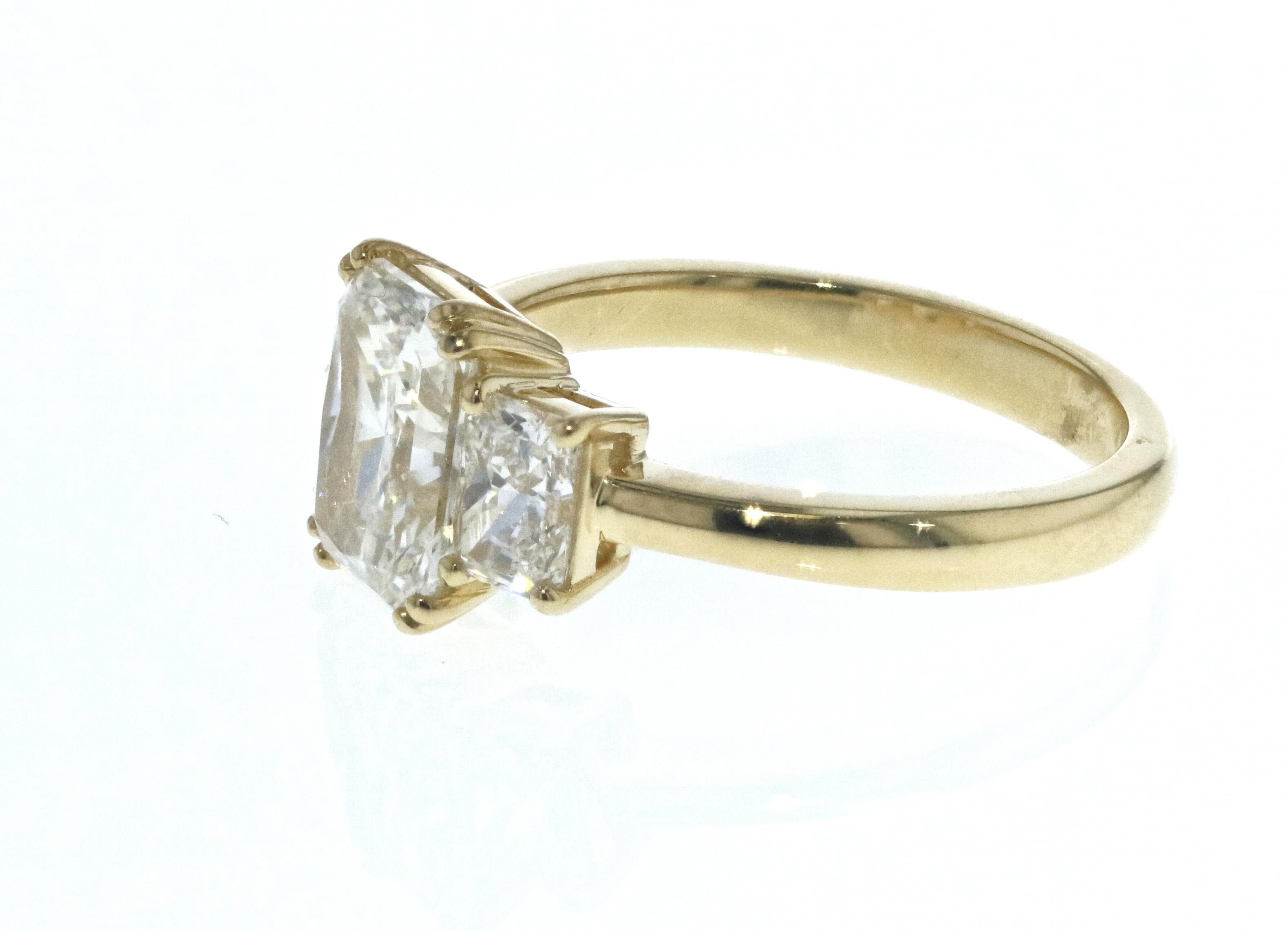 This diamond ring is crafted in 18k yellow gold, contains a Radiant Cut Diamond (1.53 total carat weight, G color, VS2 clarity,  surrounded by 2 matching Radiant Cut Diamonds (0.67 total carat weight, G color, VS clarity). With a raised profile and