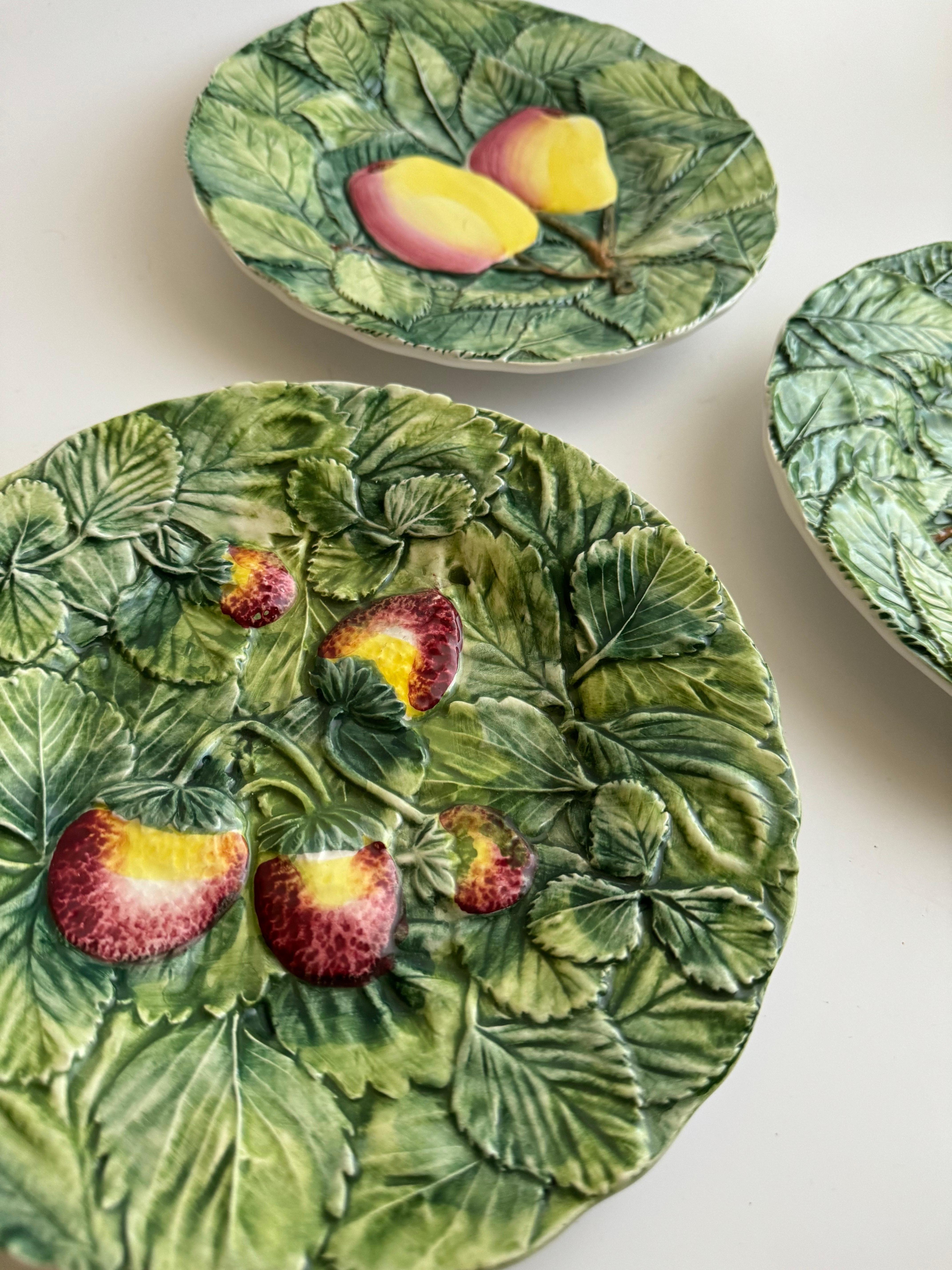 Set of three vintage Italian Majolica plates, each featuring a different embossed fruit design on a green leafy background. These decorative plates are from the 1980s and measure 13 inches in diameter. They appear to be in excellent condition