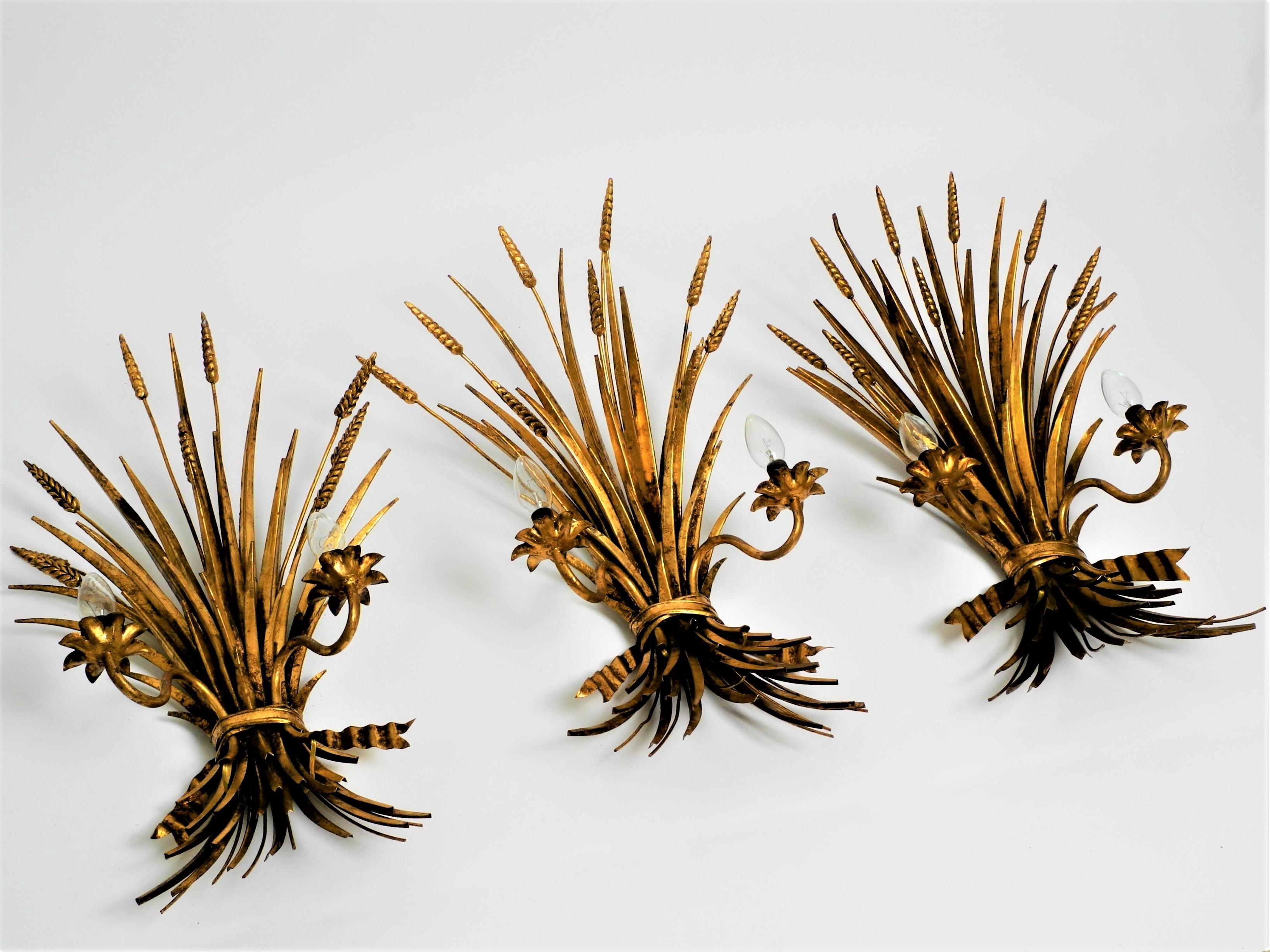 A set of three large Midcentury Hollywood Regency gilt metal sheaf of wheat wall sconces each have two candle arms. Attributed to Hans Kögl.

The lamps are made of heavy, gold-plated iron.

They have been rewired and are fully functional.

Each lamp