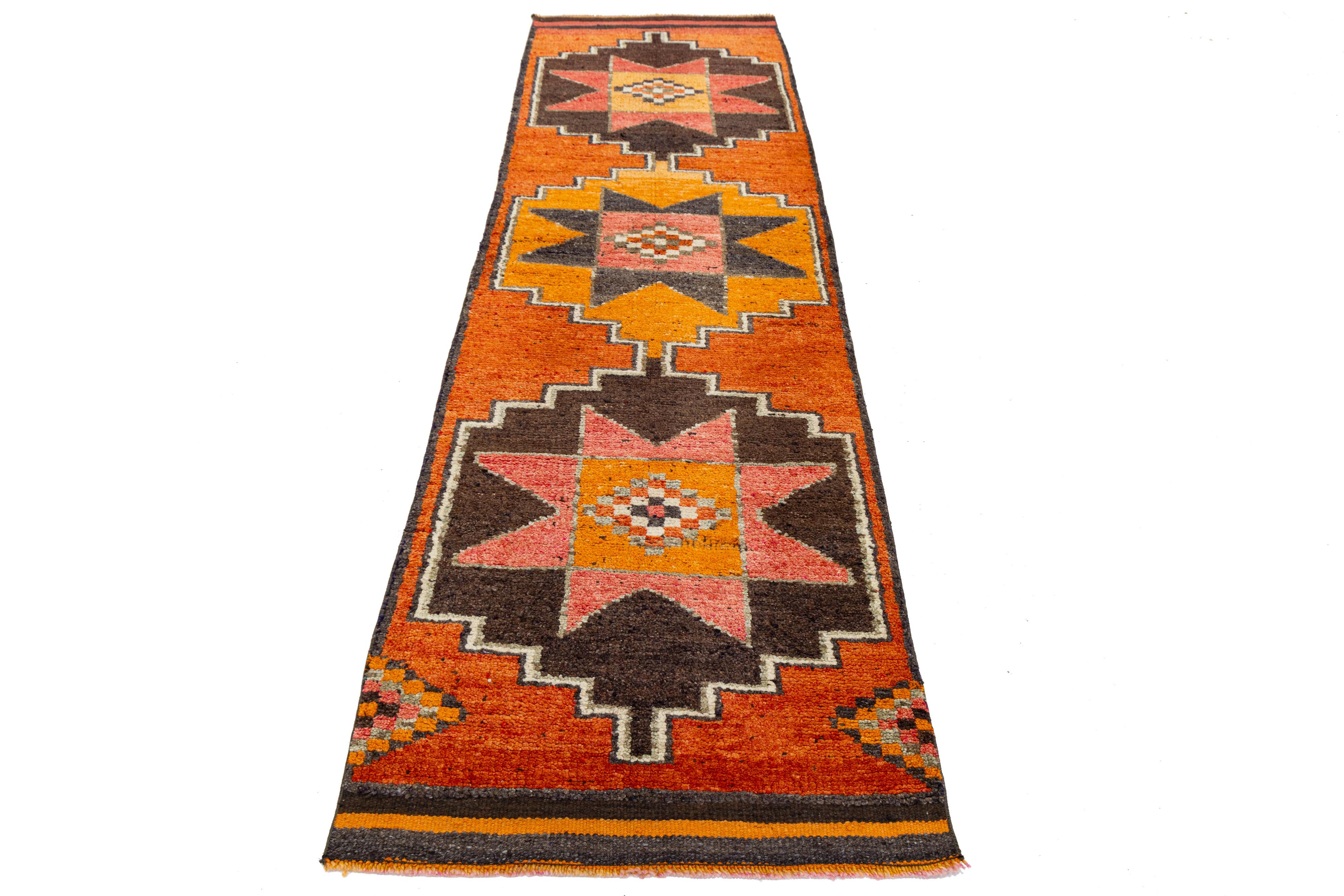 Tessuto a mano in Turchia, questo runner in lana vintage presenta audaci medaglioni geometrici e una tavolozza calda e terrosa ispirata ai disegni tradizionali dell'Anatolia. La sua forma allungata e l'estetica di metà secolo la rendono un accento