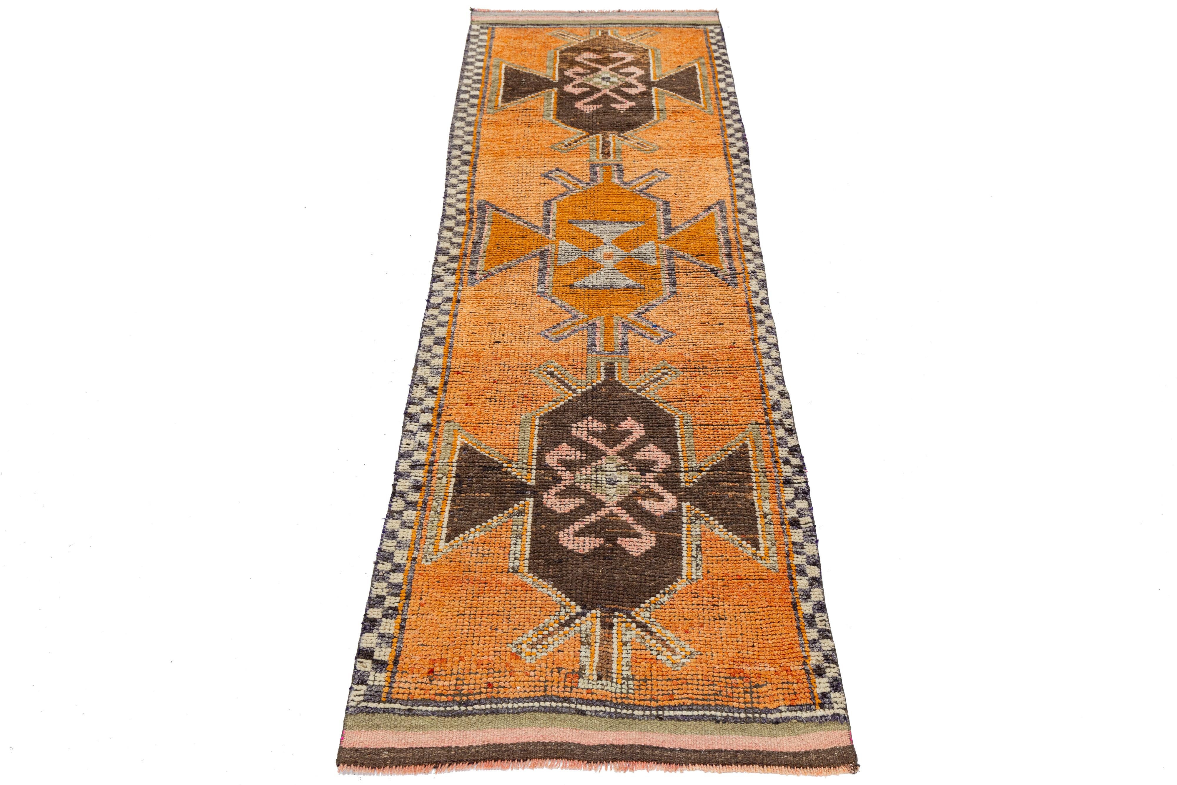 Dieser in der Türkei handgewebte Vintage-Läufer spiegelt die geometrische Eleganz und die erdige Farbpalette des anatolischen Designs aus der Mitte des 20. Die kühnen Medaillons und Stammesmotive aus natürlicher Wolle versprühen Vintage-Charme mit