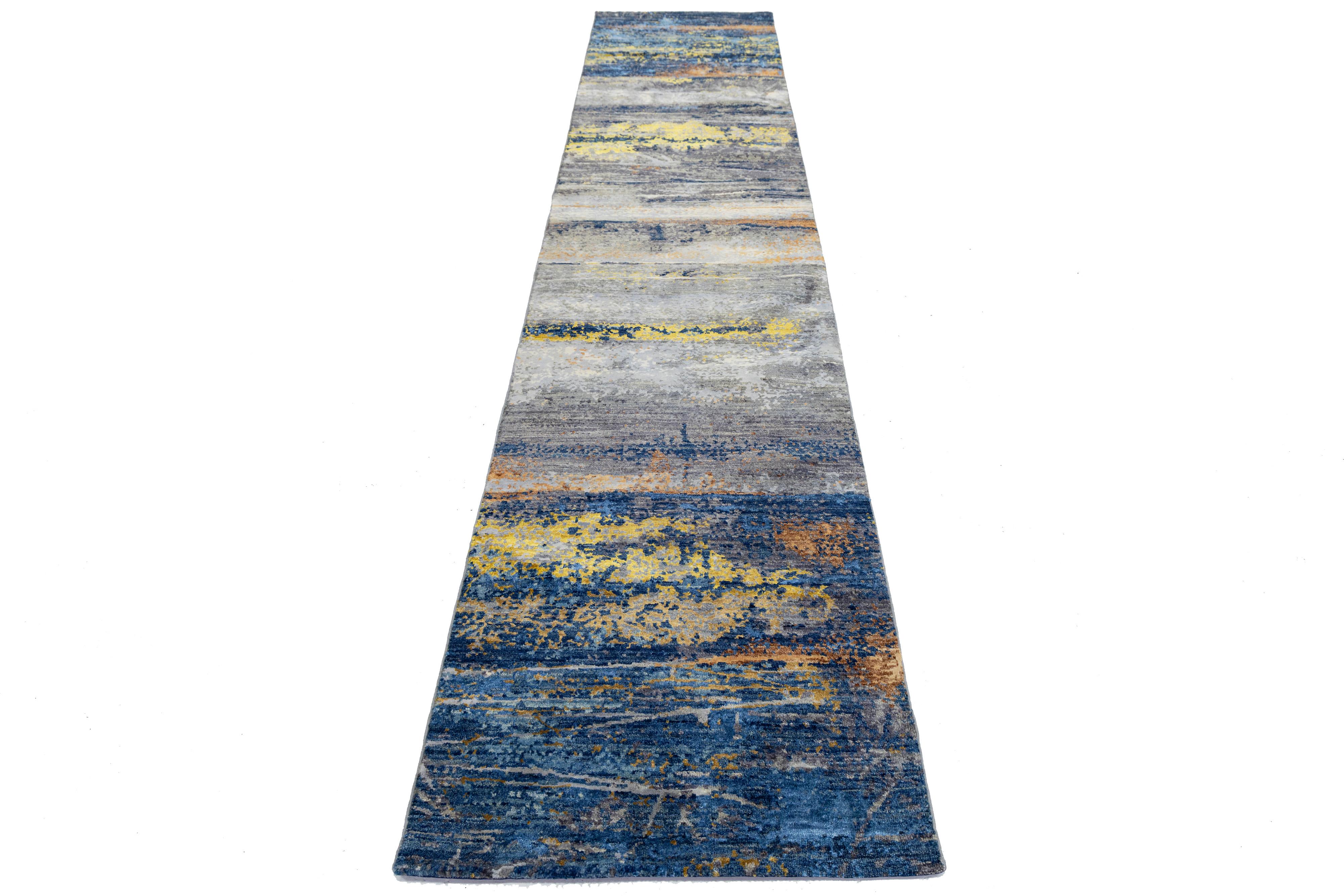 Dieser moderne, handgeknüpfte Teppich besticht durch sein abstraktes Design und seine lebendige Farbpalette. Der Hintergrund aus hochwertiger Wolle oder Seide ist in Grau, Blau, Braun und Gold gehalten und hebt das filigrane Muster hervor, das jedem