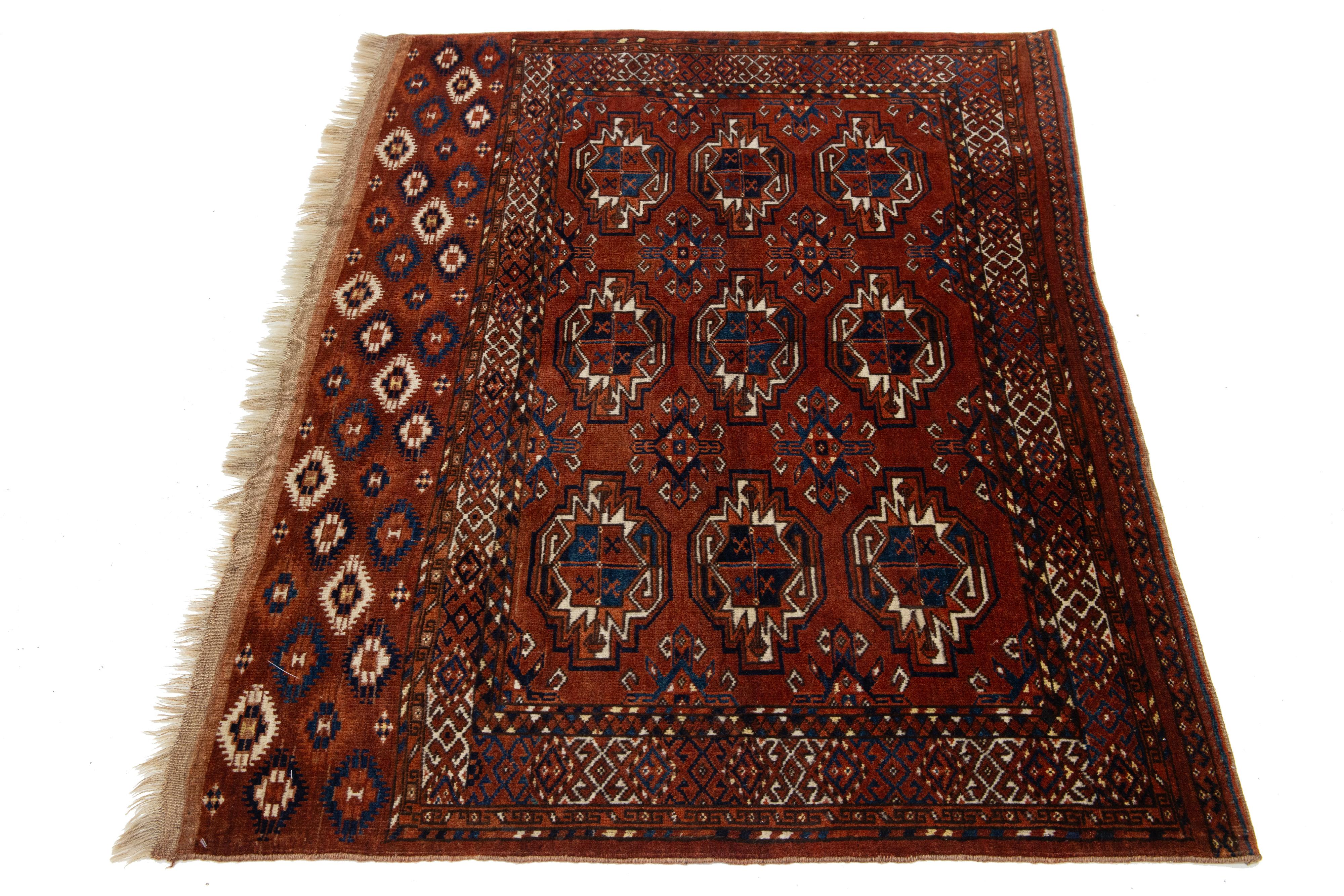 The vintage hand-knotted wool rug from Turkmen features a red-rust color field, navy blue, beige, and orange accents, and fringes in an intricate geometric pattern.

This rug measures 3'8