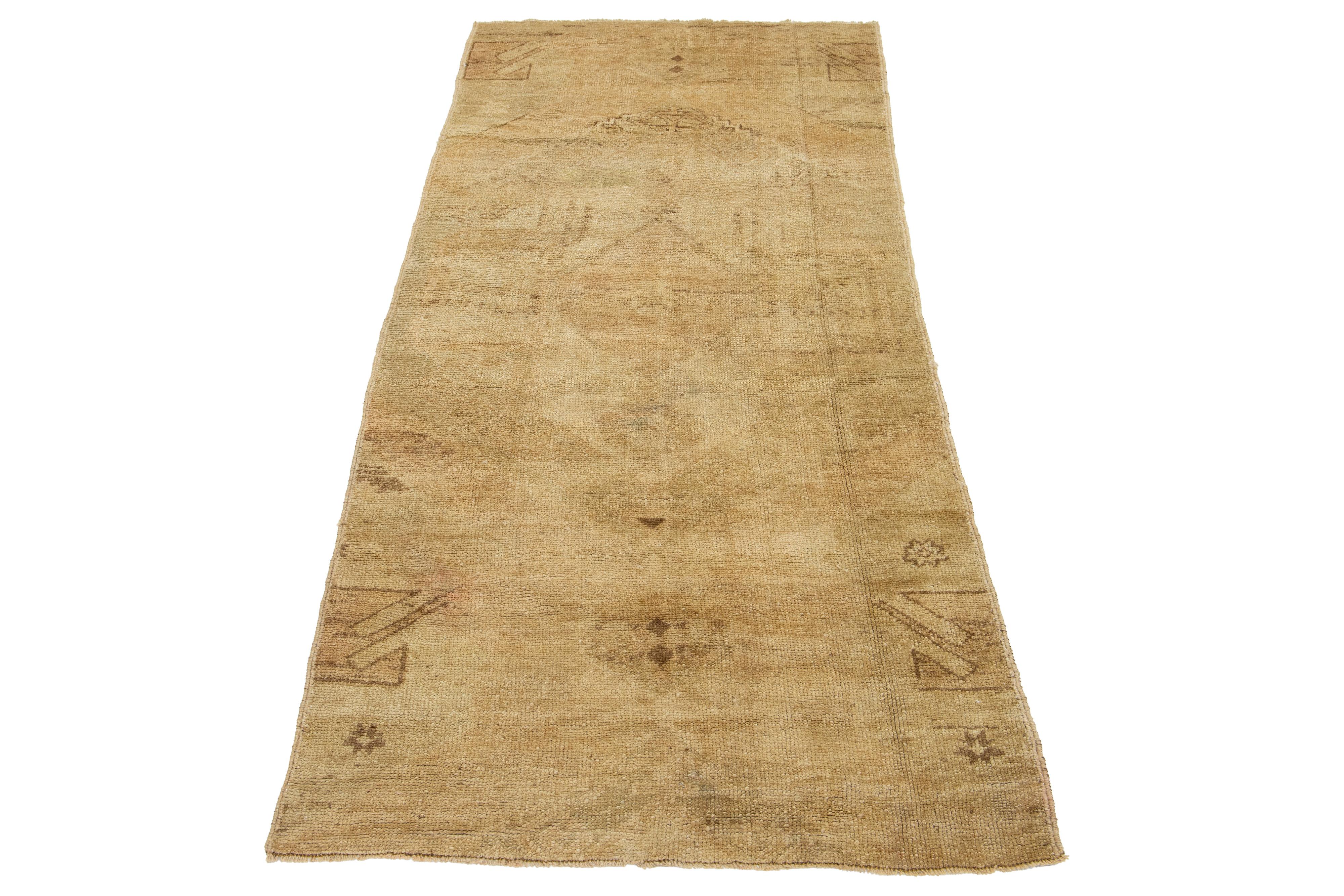 Ein wunderschöner türkischer Teppich im Vintage-Stil zeigt ein hellbraunes Feld mit einem geometrischen Stammesmuster, das sich über den gesamten Teppich erstreckt und von Brauntönen akzentuiert wird.

Dieser Teppich misst 2'11