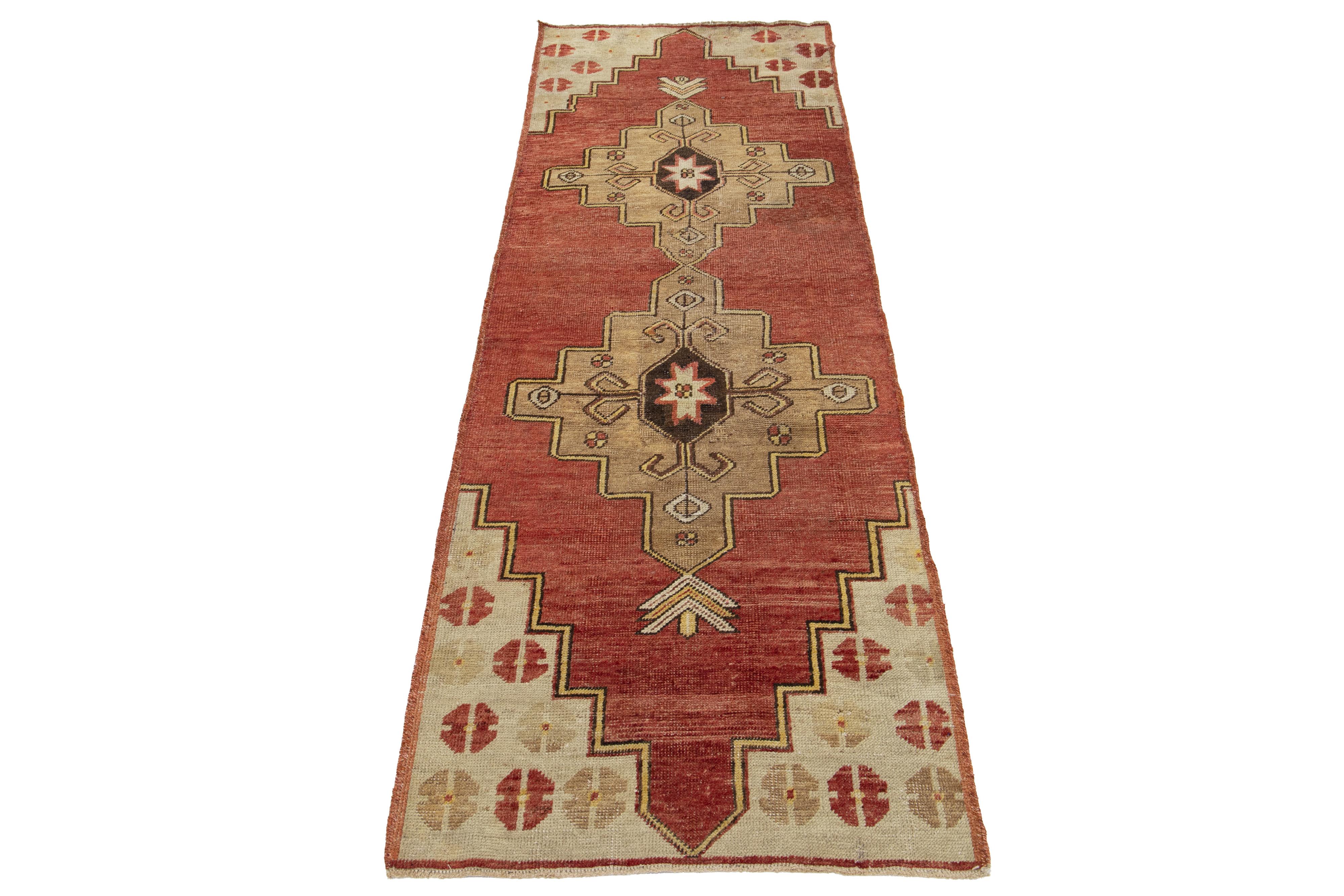 Ce magnifique tapis de course turc vintage présente un riche champ rouge-rouille, élégamment orné d'un captivant motif géométrique tribal qui s'étend sur l'ensemble du tapis. Le design est encore accentué par des accents vibrants dans une variété de
