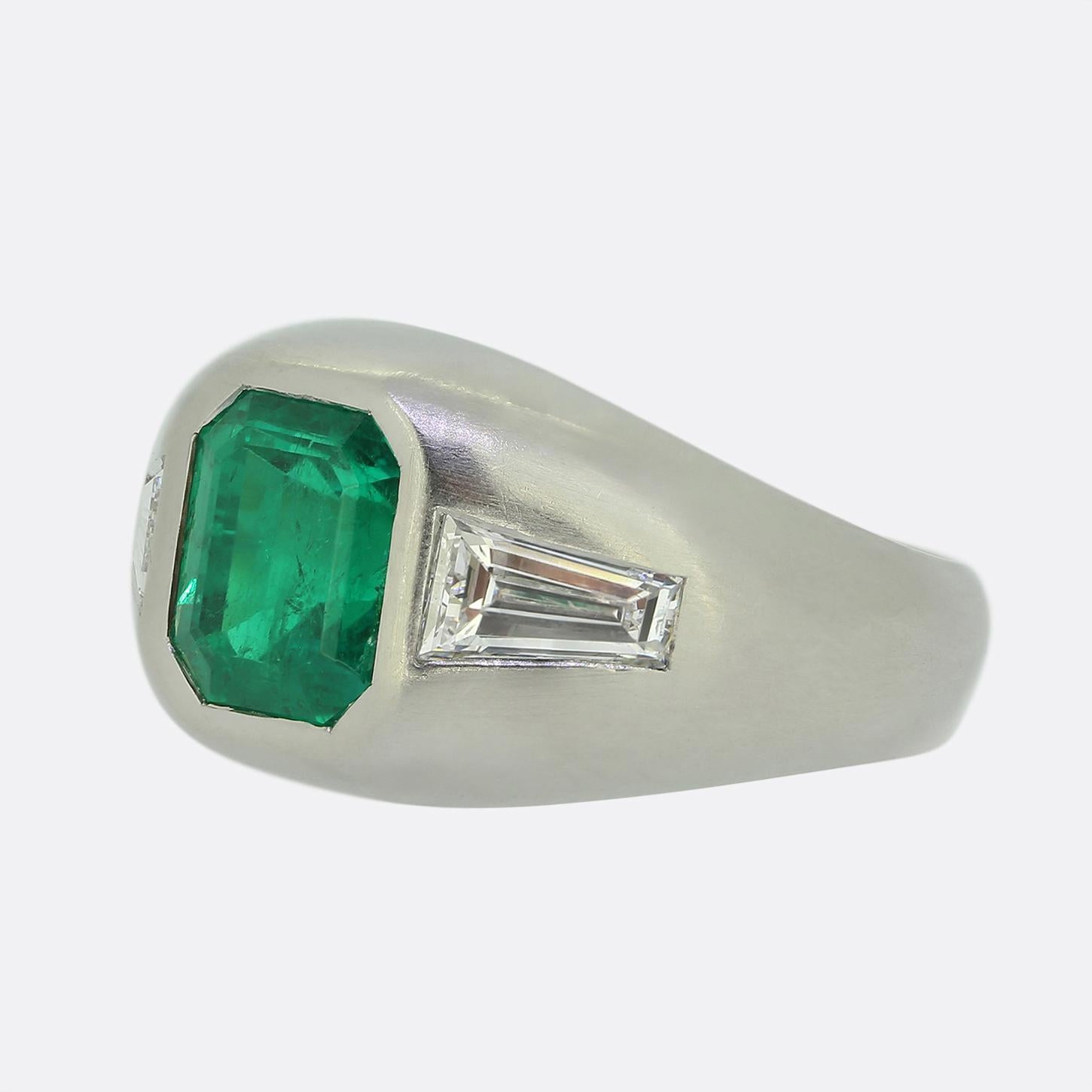 Hier haben wir einen raffinierten Ring mit drei Steinen, in dessen Mittelpunkt ein lebendiger Smaragd von 3,00 Karat kolumbianischer Herkunft steht. Dieser auffällige grüne Edelstein ist elegant in der Mitte des Zifferblatts gefasst und wird auf