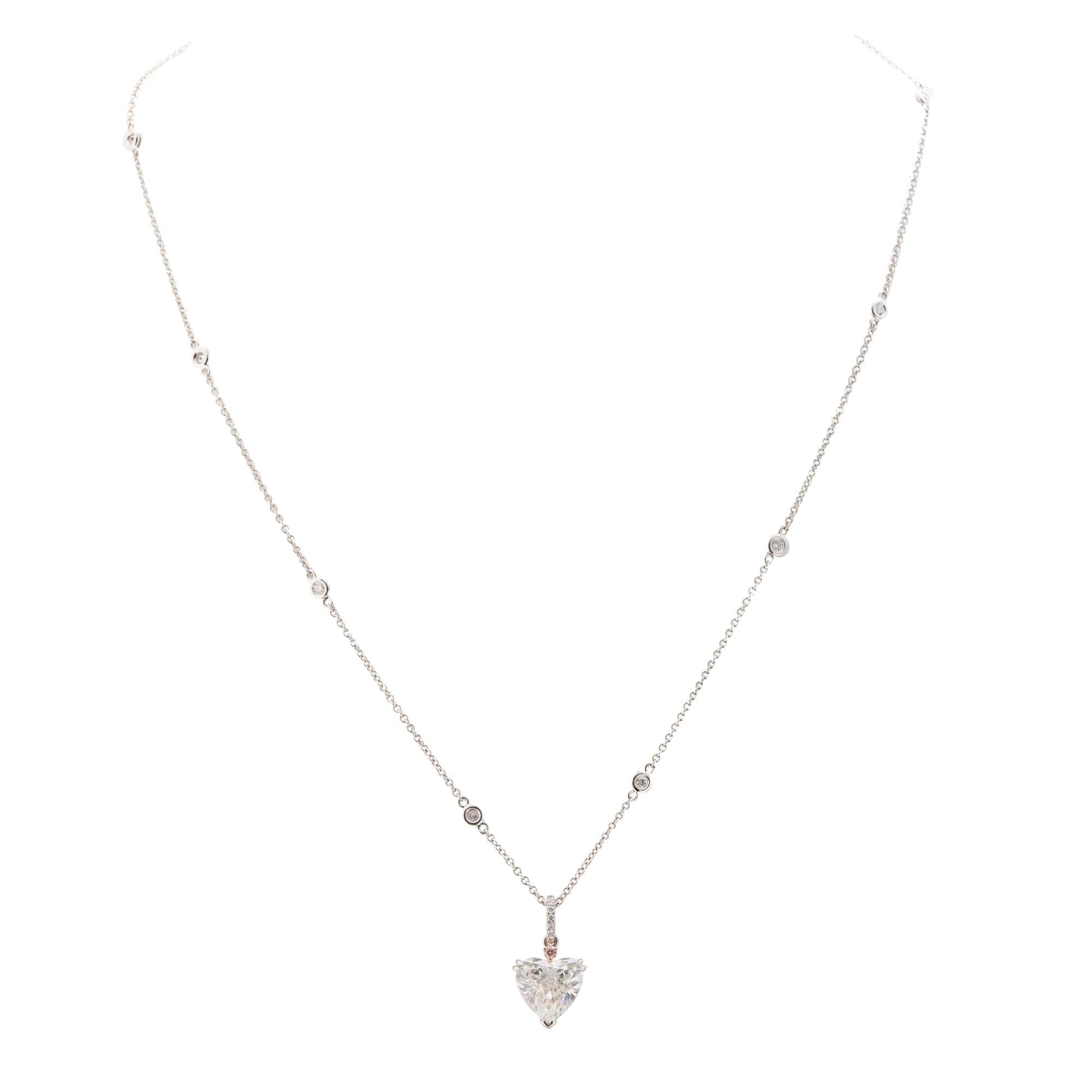 18 karat white and rose gold pendant consisting of one heart shaped diamond weighing 3.00 carats accented with two round pink diamonds one  weighing .02 carats and one weighing .03 carats. Round brilliant cut diamonds accent the bail and chain with