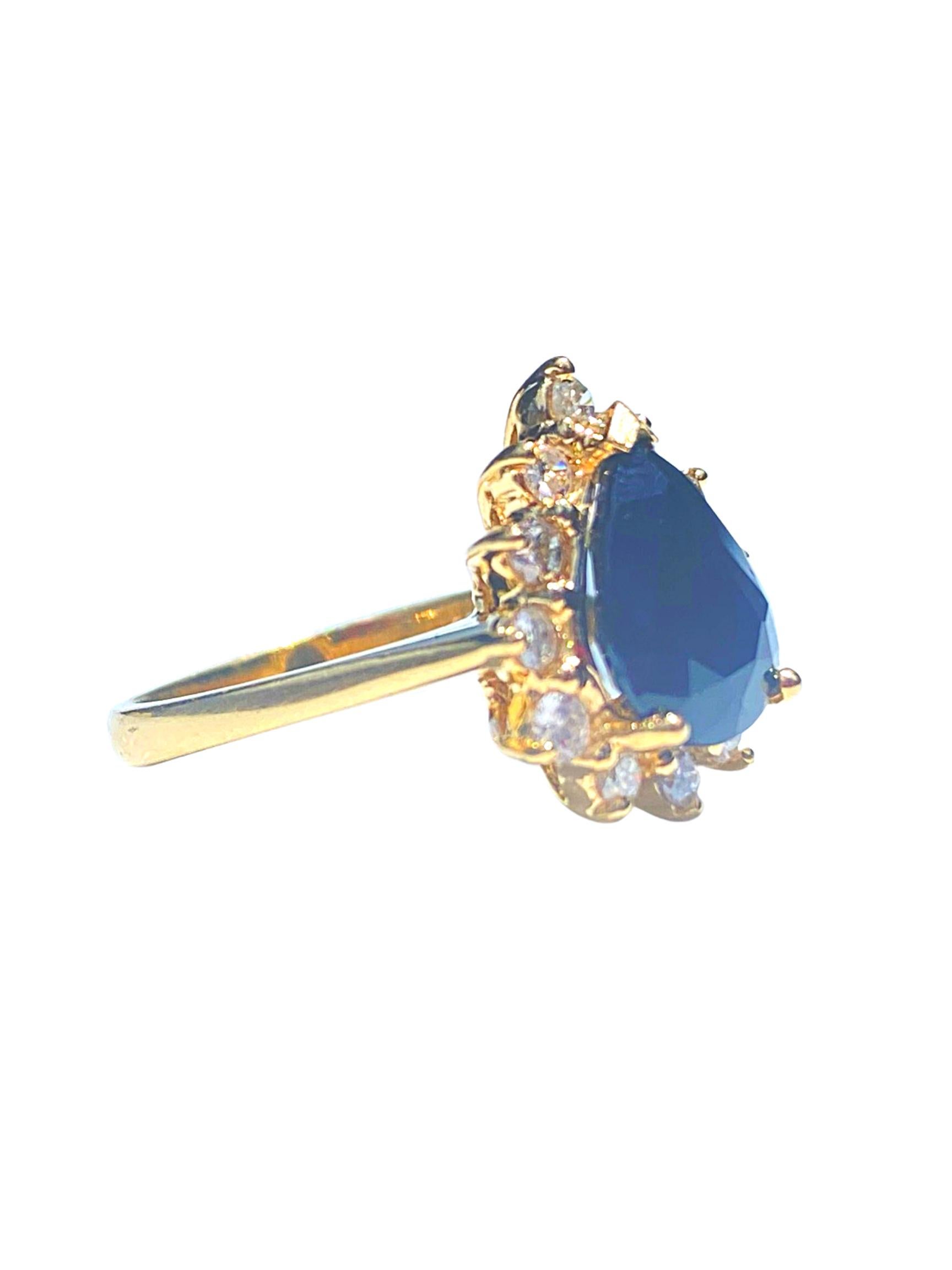 Centering an approximately ~3.00 Carat Pear-Shape Blue Diamond, framed by an additional 12 Round-Brilliant Cut Diamonds, and set in 14K Yellow Gold. 

Details:
✔ Stone: Blue Sapphire
✔ Center-Stone Weight: ~3.00 Carats
✔ Stone Cut: Pear
✔ Stone