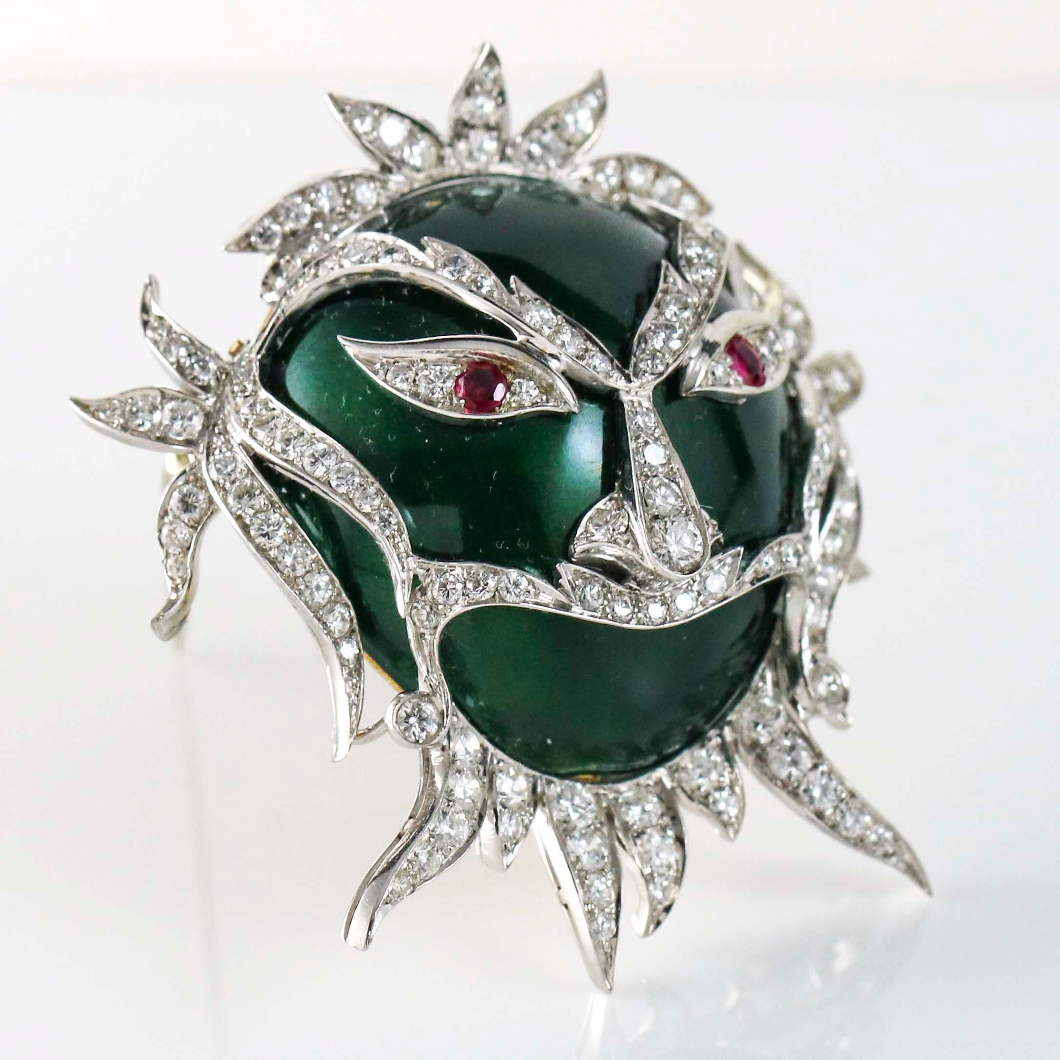Carnival ornate face mask brooch crafted in 18k white and yellow gold with green enamel, ruby eyes and diamond details. Diamond total carat weight, 3 carats.