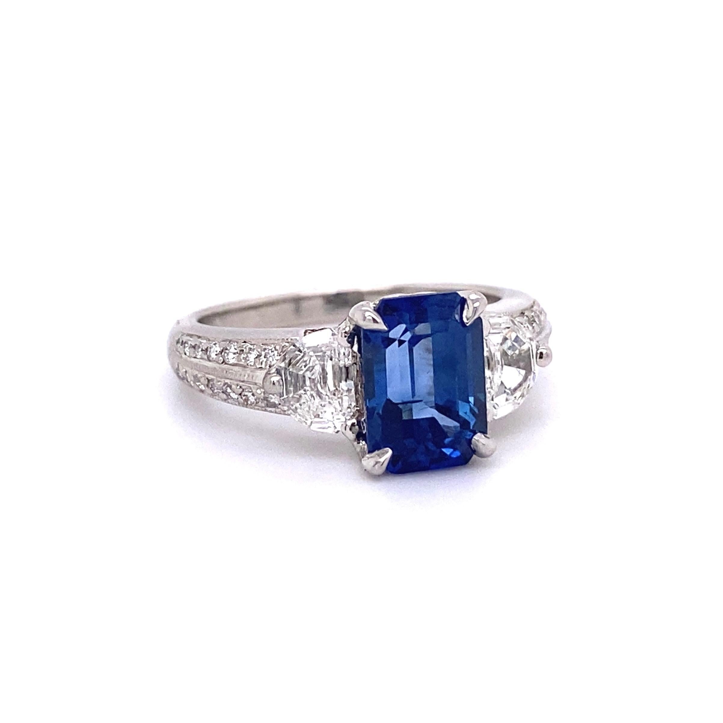 Beautiful finely detailed Platinum 3 Stone Blue Sapphire and Diamond Ring. Securely Hand set with a 3.00 Carat Emerald-cut Blue Sapphire and 2 Diamonds approx. 0.94tctw. The Sapphire is a Beautiful Royal Blue Color and eye clean. The diamonds are F