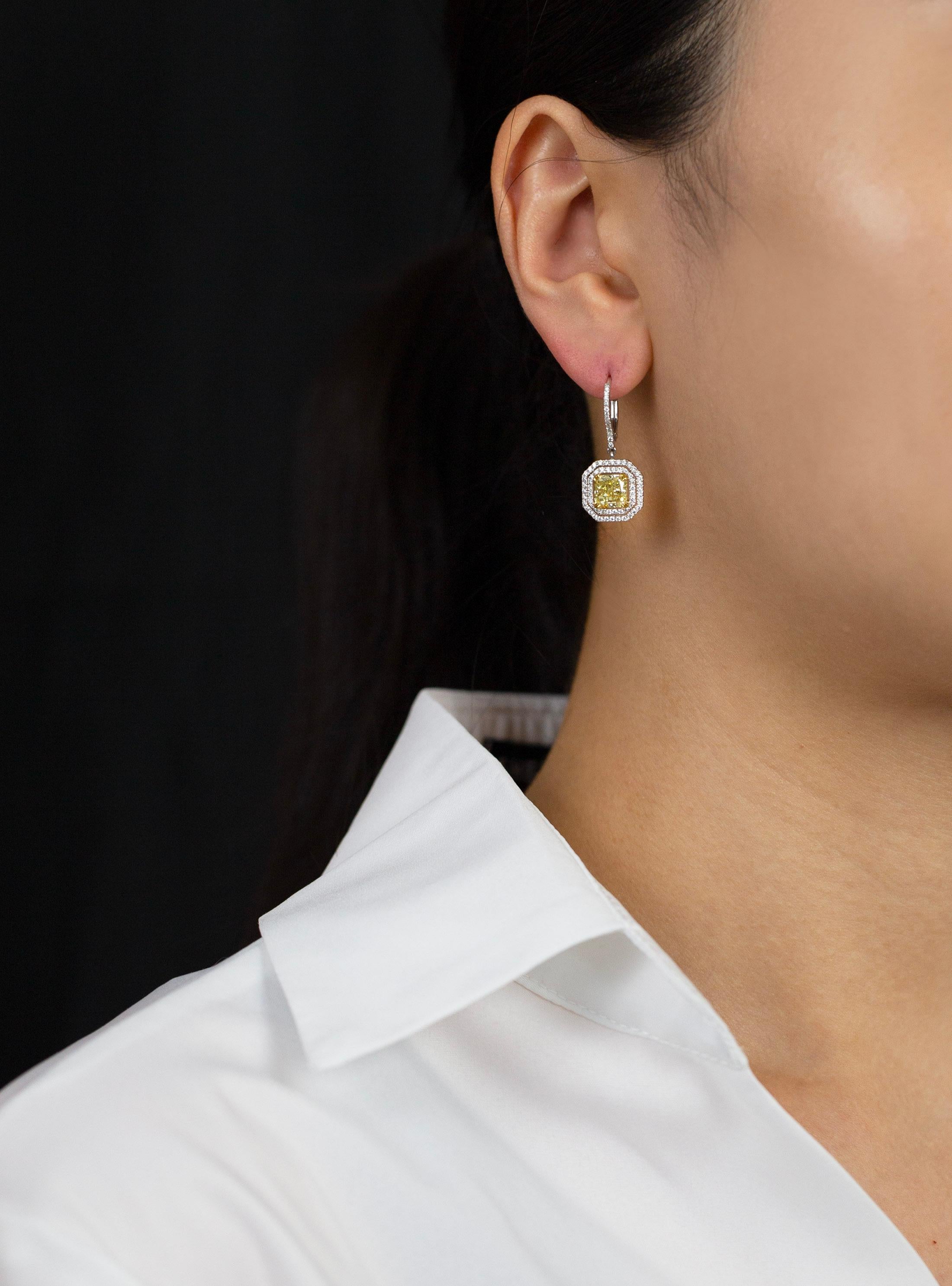 A beautiful and color-rich pair of dangle earrings showcasing radiant cut diamonds weighing 1.50 carats each, certified by GIA as fancy light yellow color and SI1-VS2 in clarity respectively. Surrounded by double row of brilliant round diamonds in a