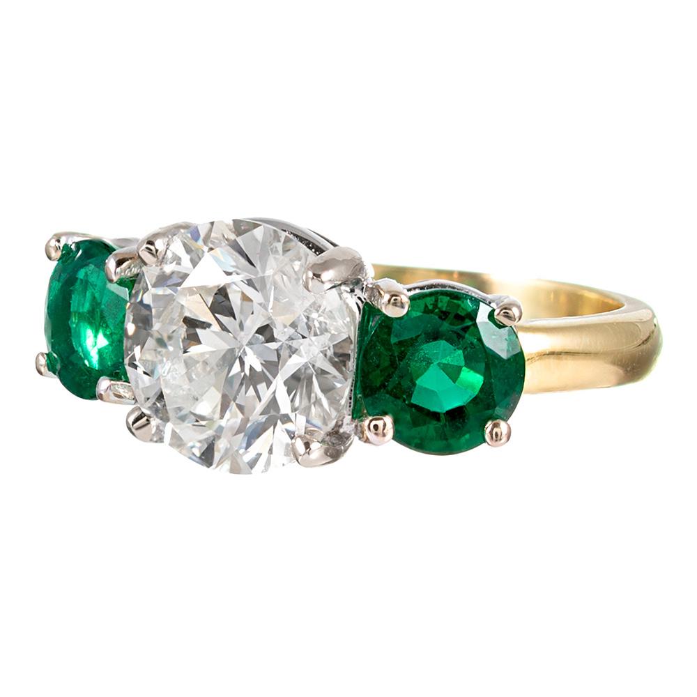 A gorgeous trio of gemstones assembled into classic perfection, the 3.01 carat round brilliant diamond sits in platinum flanked by a round emeralds. The diamond is graded I-J color and Vs2-Si1 clarity while the emeralds weigh 1.50 carats combined