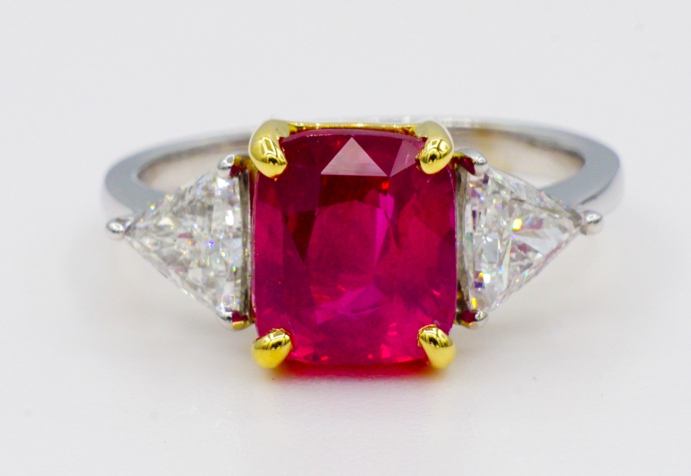 Stunning 18kt yellow gold two-tone ring with a natural GIA certified 3.01ct cushion cut ruby accented with two trilliant cut diamonds that are .80cttw. 

The ruby measurement is 8.32 x 7.2 x 5.00 mm and has GIA report #6227370047. The ruby is in a