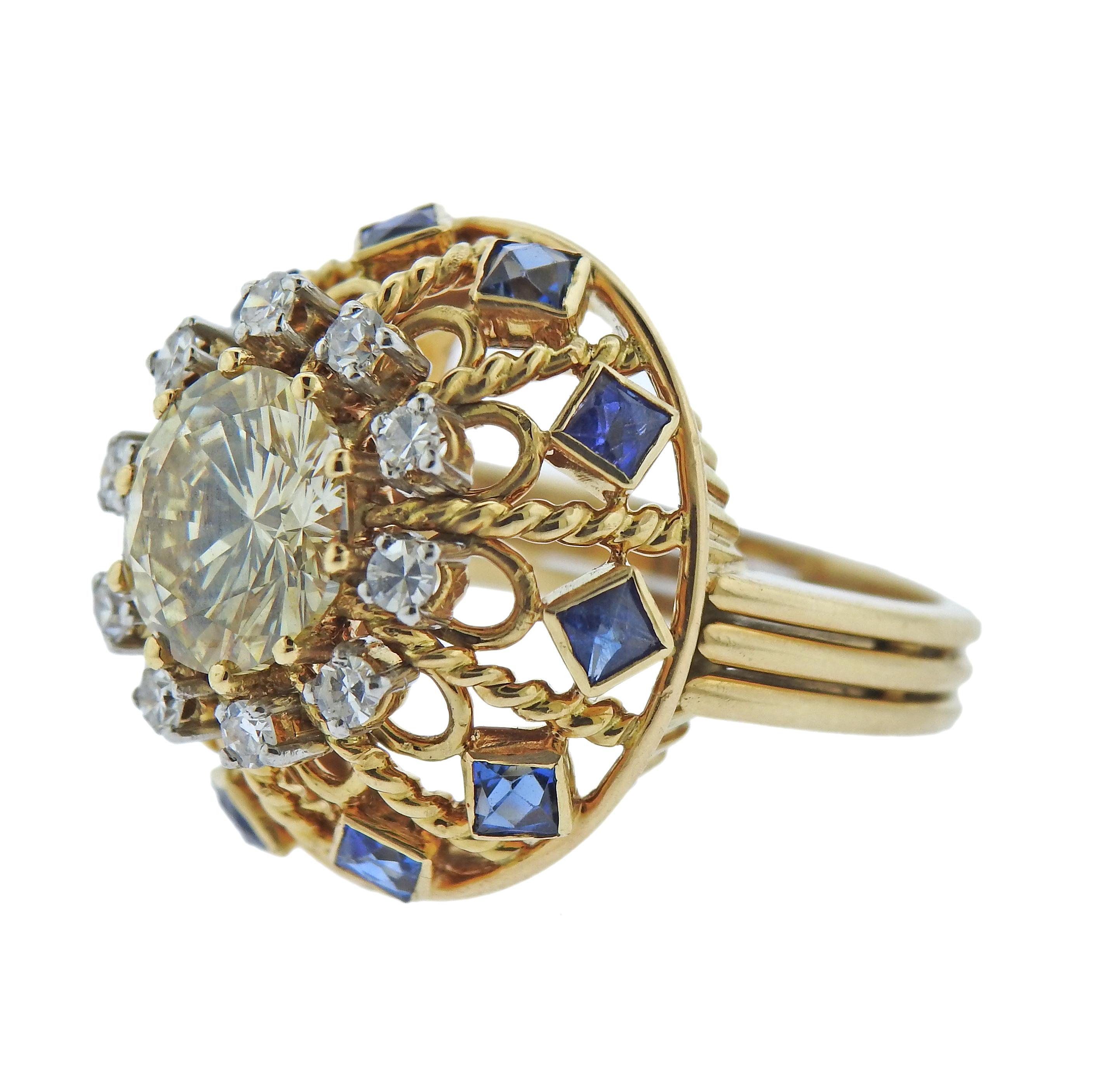 18k gold ring, set with center approx. 3.02ct round brilliant diamond, surrounded with blue sapphires and approx. 0.30ctw in diamonds. Ring size - 6, ring top - 22mm in diameter. Weight - 12.9 grams. 