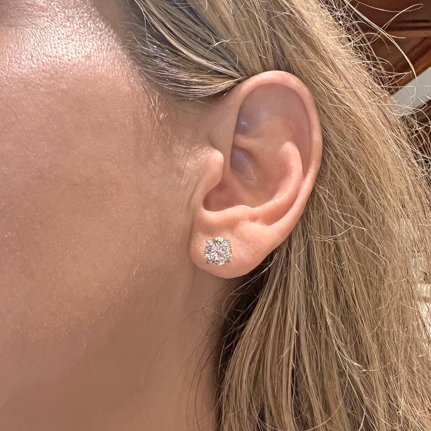 Round brilliant-cut diamond stud earrings, showcasing a pair of well-matched colorless diamonds weighing 3.02 total carats, the diamonds secured in four-prong platinum martini settings with posts for pierced ears. Both diamonds are F-color and