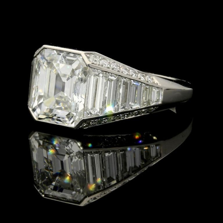 A stunning emerald cut diamond ring by Hancocks, centred with a beautiful vintage- emerald-cut diamond weighing 3.02cts and of G colour and VS1 clarity within a rubover setting to elegantly tapering shoulders set with a line of calibre cut baguette
