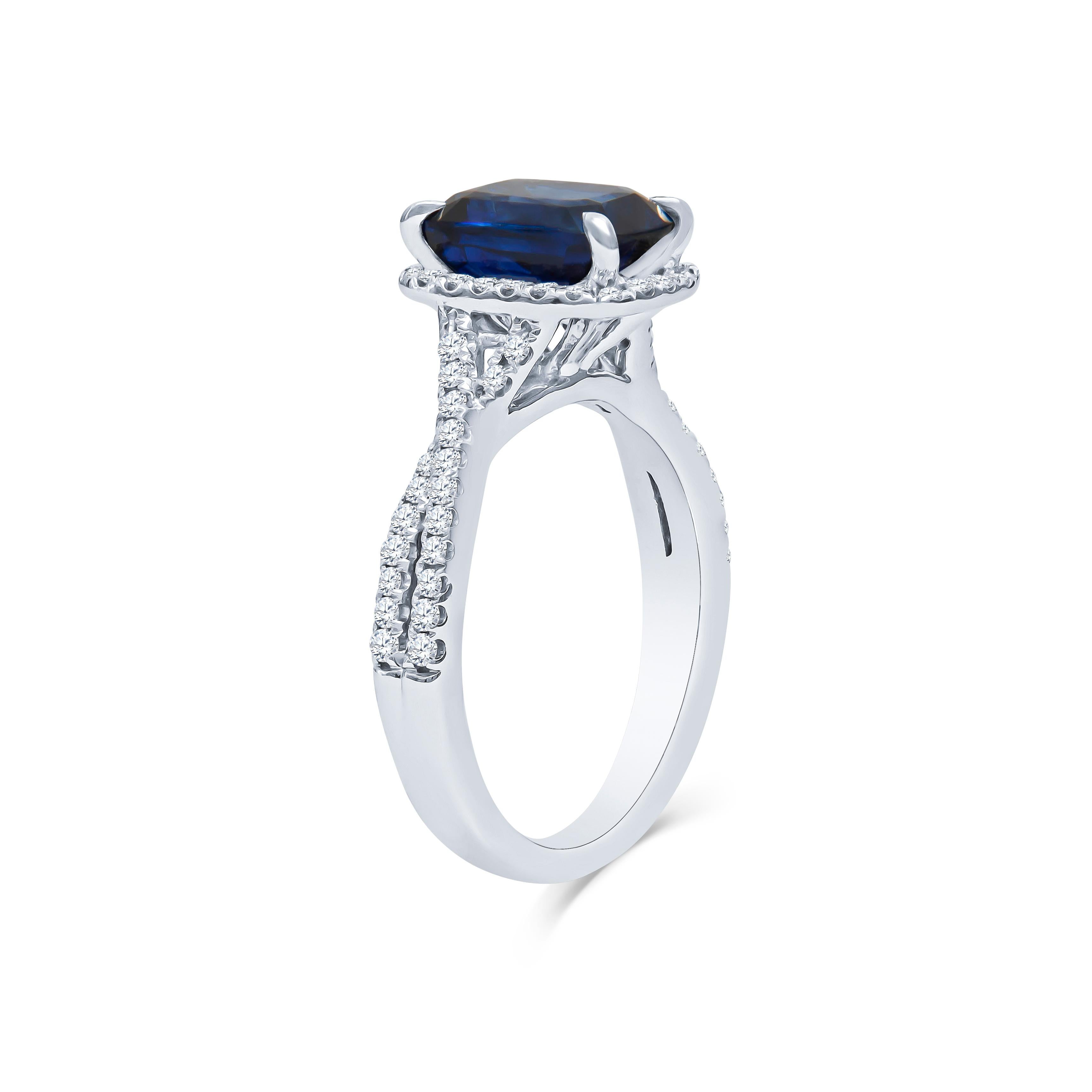 Creative and expertly hand-crafted; A dazzling halo set with a 3.04 carat cushion cut natural royal blue sapphire set in an 18K white gold diamond setting that carries 0.40 carats total of round brilliant diamonds. The sapphire is a lovely, rich