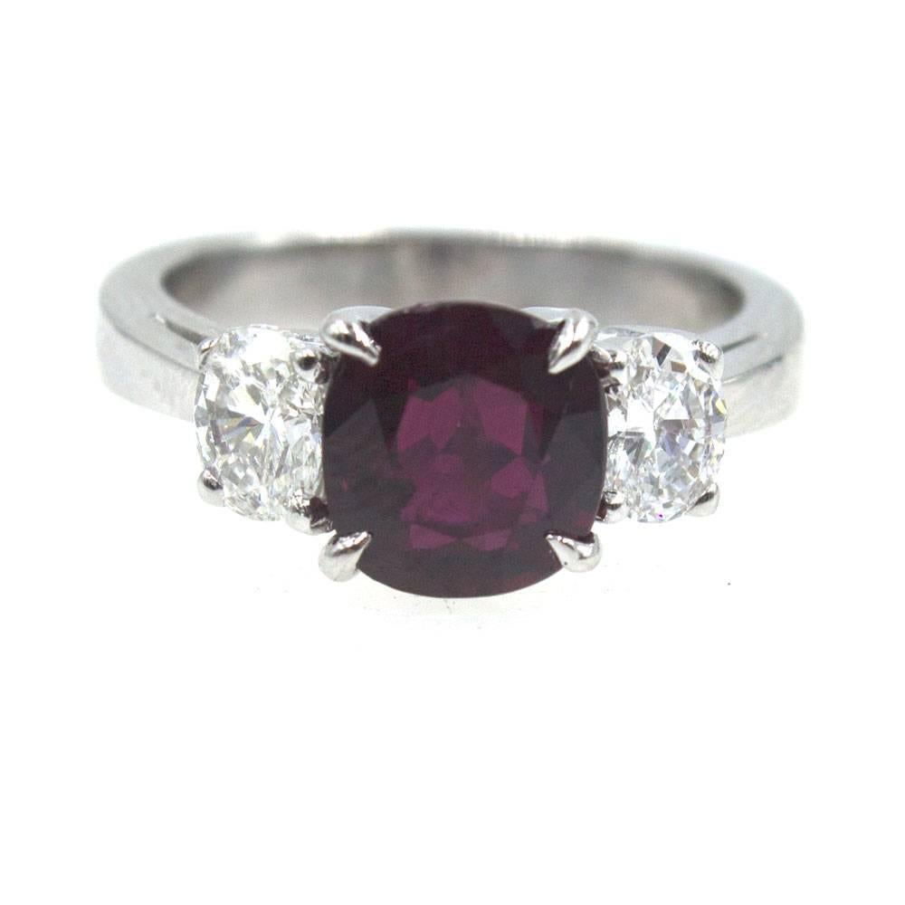 Beautiful platinum three stone ring featuring a 3.04 carat cushion cut Ruby. The ruby is flanked on either side by 1.00 carat total weight of round brilliant cut diamonds. The diamonds are H color and VS2-SI1 clarity. 
GIA Certificate Number: