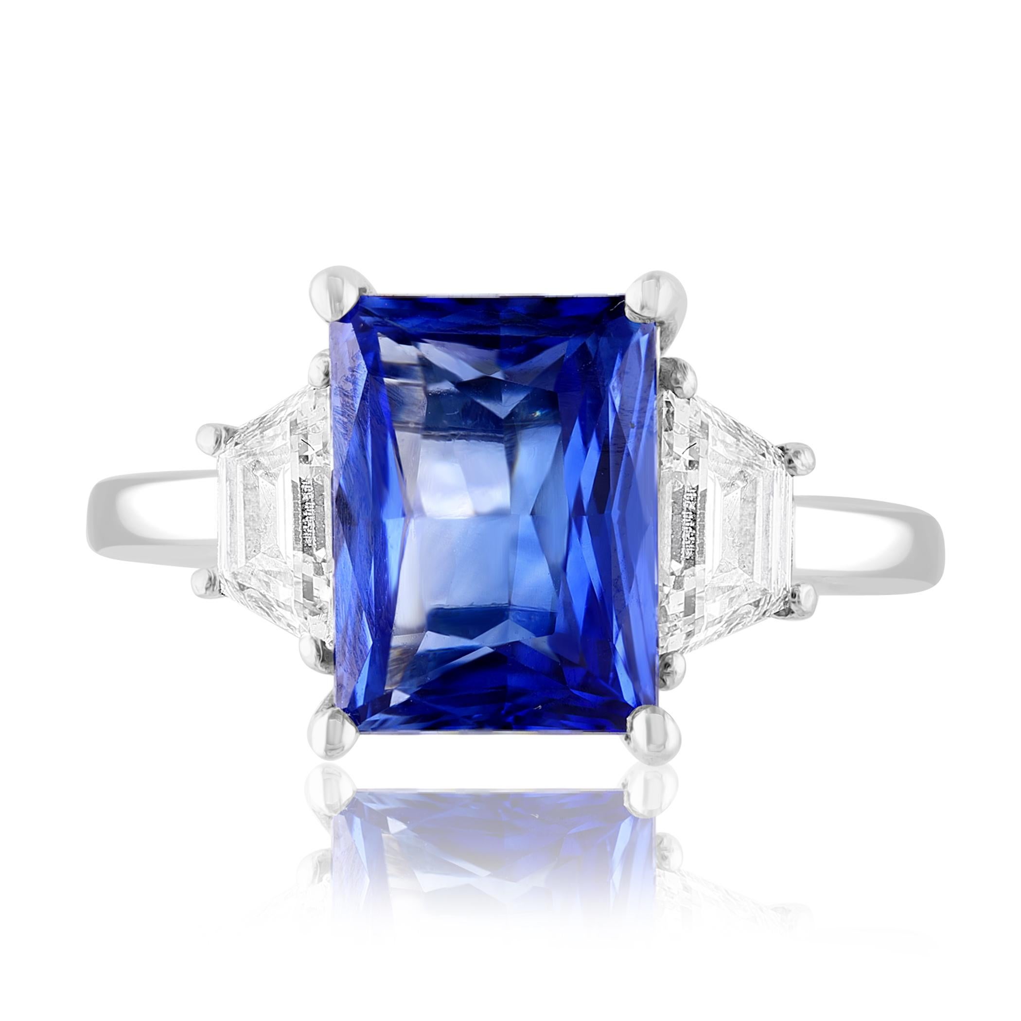 Showcasing Emerald cut, Vibrant color Blue Sapphire weighing 3.06 carats, flanked by two brilliant cut trapezoid diamonds weighing 0.92 carats total. Elegantly set in a polished platinum composition.