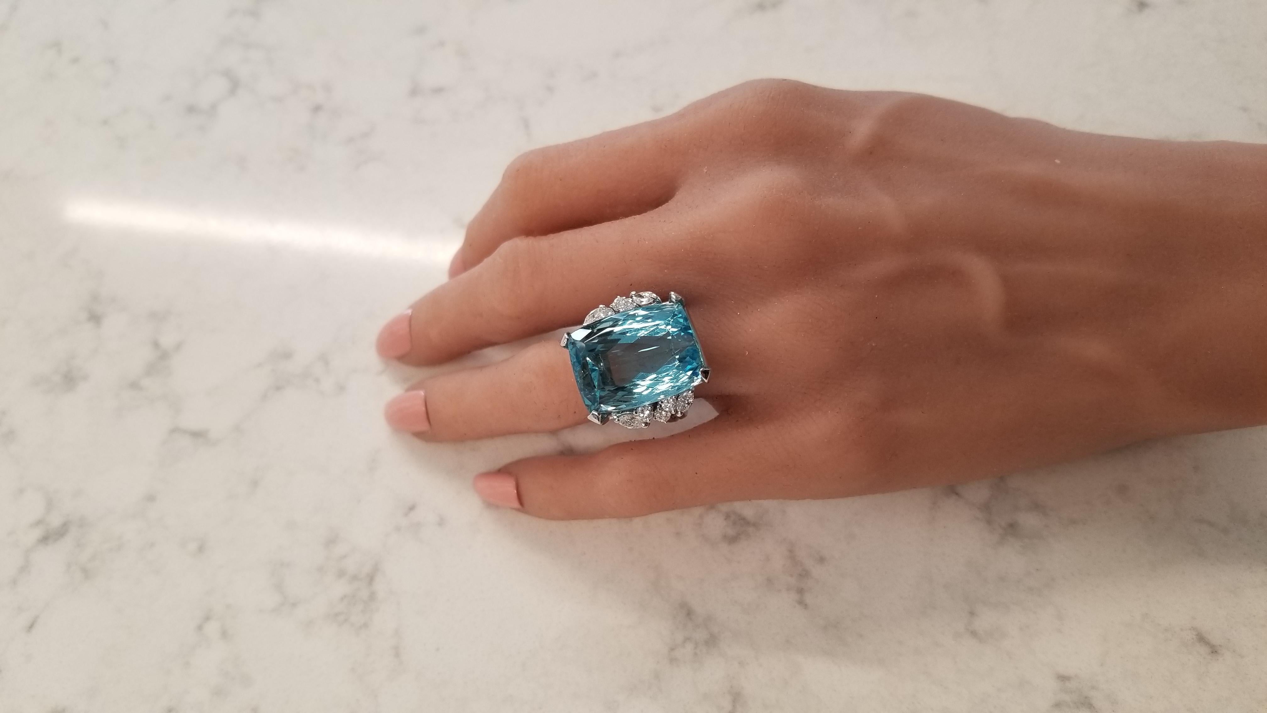 This is a significant cocktail ring that features a clear, crisp emerald cut aquamarine weighing 30.63 carats and measures 20.44 x 15.45mm and exhibits the color of sky blue or glacial water. The gem source is Brazil; its transparency and clarity