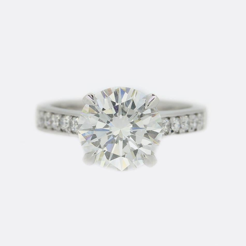 This is a wonderful platinum diamond engagement ring. The round brilliant cut diamond is an impressive 3.07 carats and sits in a raised 4 clawed mount. Each shoulder is set with 6 round brilliant cut diamonds that are perfectly matched for colour