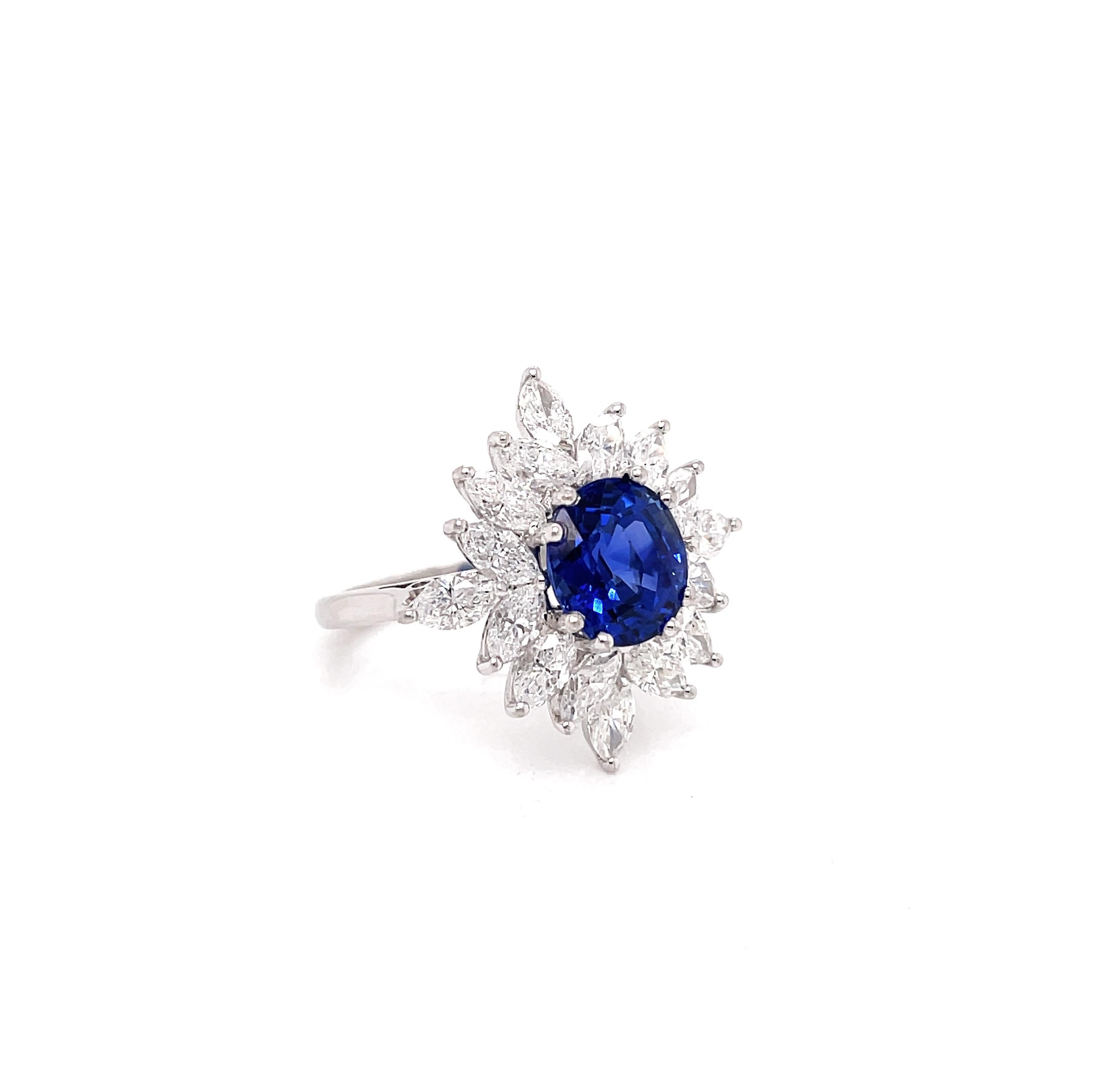 This gorgeous vintage cluster ring is set with a royal blue oval sapphire weighing 3.09ct mounted in an eight claw, open back setting. The gemstone is perfectly set in the centre of a beautiful cluster of 16 marquise shaped diamonds weighing an