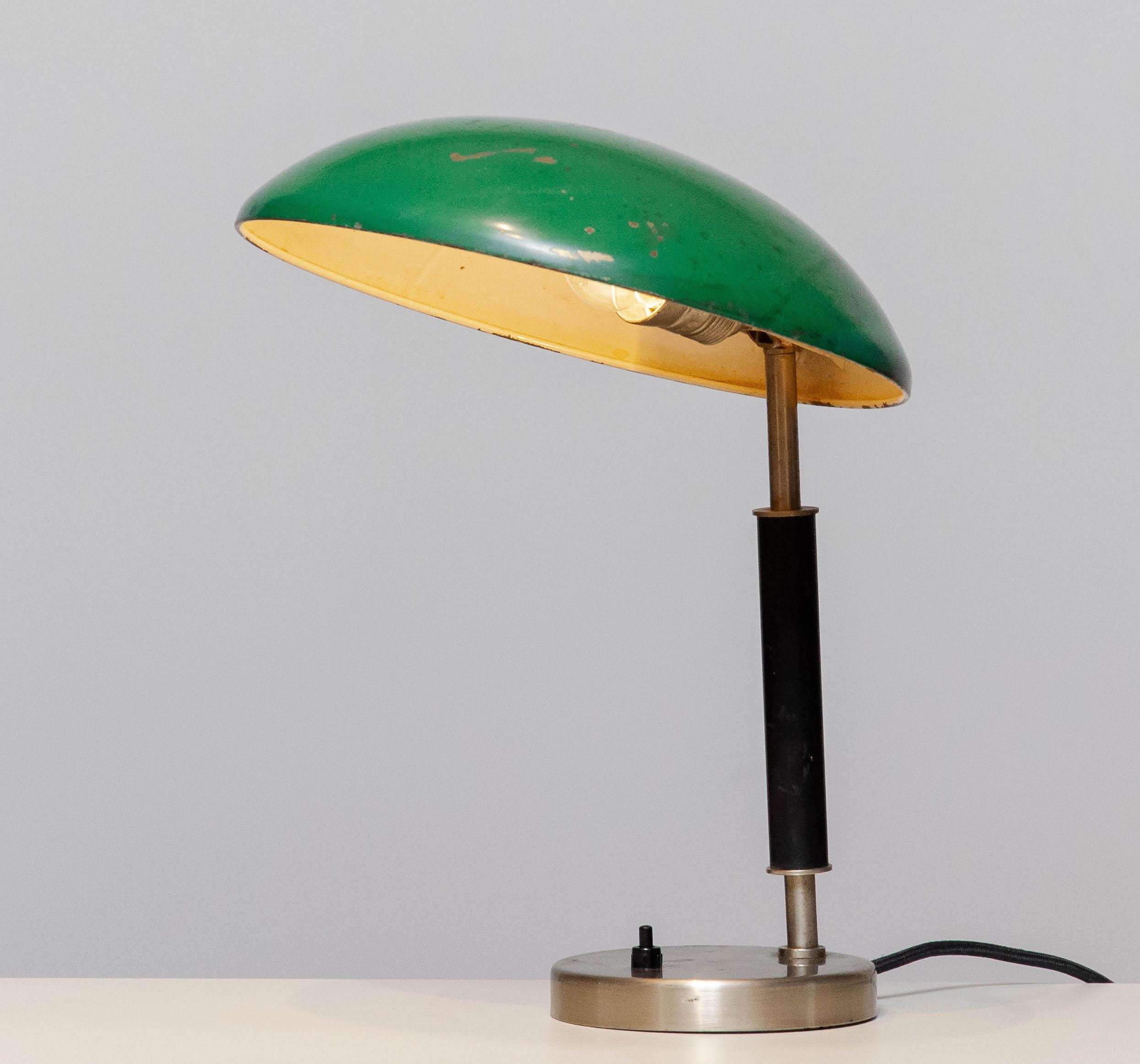 Schöne industrielle Tischlampe / Schreibtischlampe aus den 1930er Jahren, entworfen von Harald Notini für Arvid Böhlmarks Lampfabrik AB Stockholm Schweden.
Der grün lackierte Schirm ist aus Messing und hinter der klaren Metallabdeckung des Sockels
