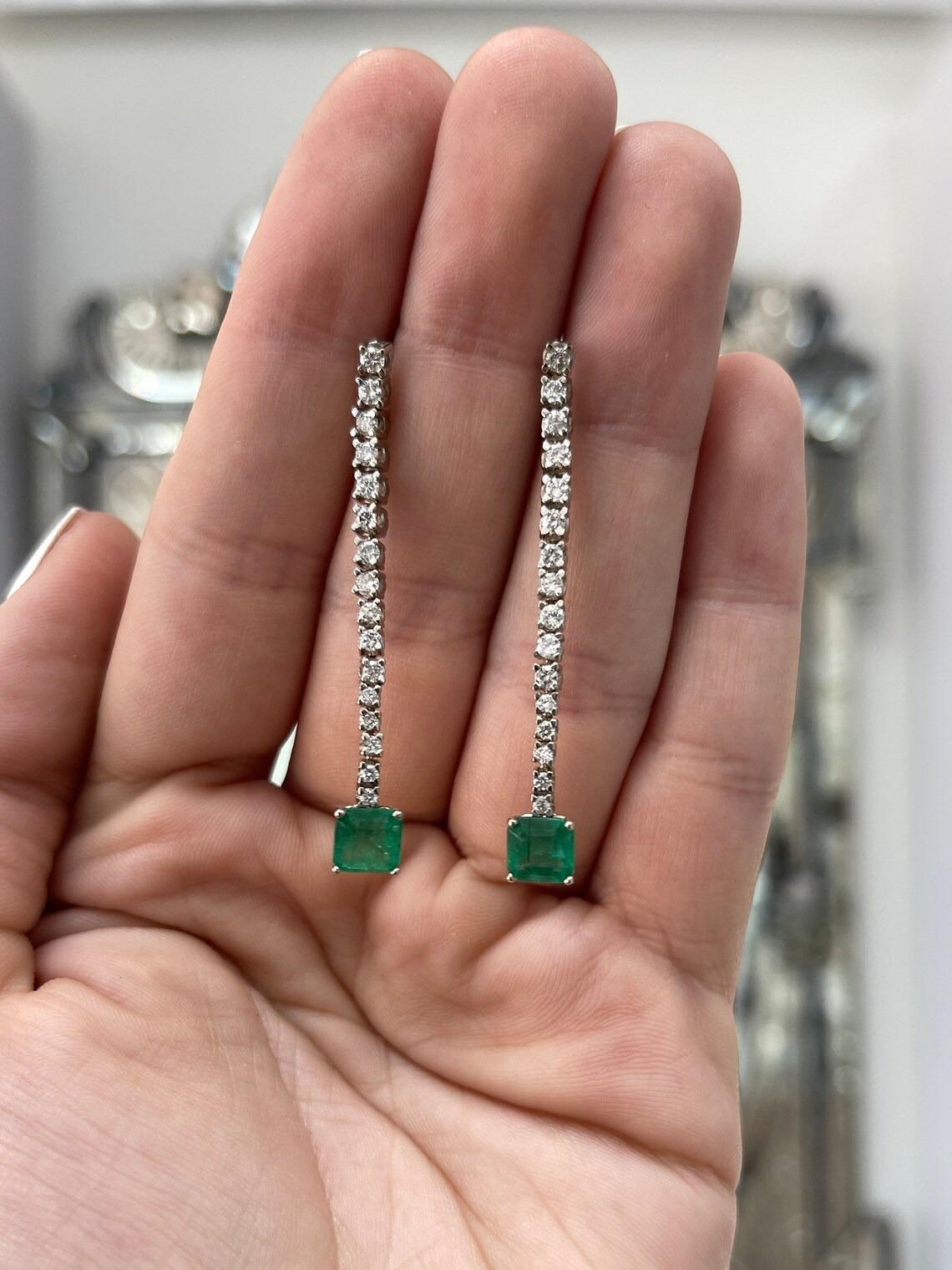 Indulge in the timeless allure of these stunning emerald and diamond dangle drop earrings. The journey begins with a cascade of brilliant round cut diamonds, leading to the grand finale of mesmerizing asscher-cut natural emeralds, each weighing over