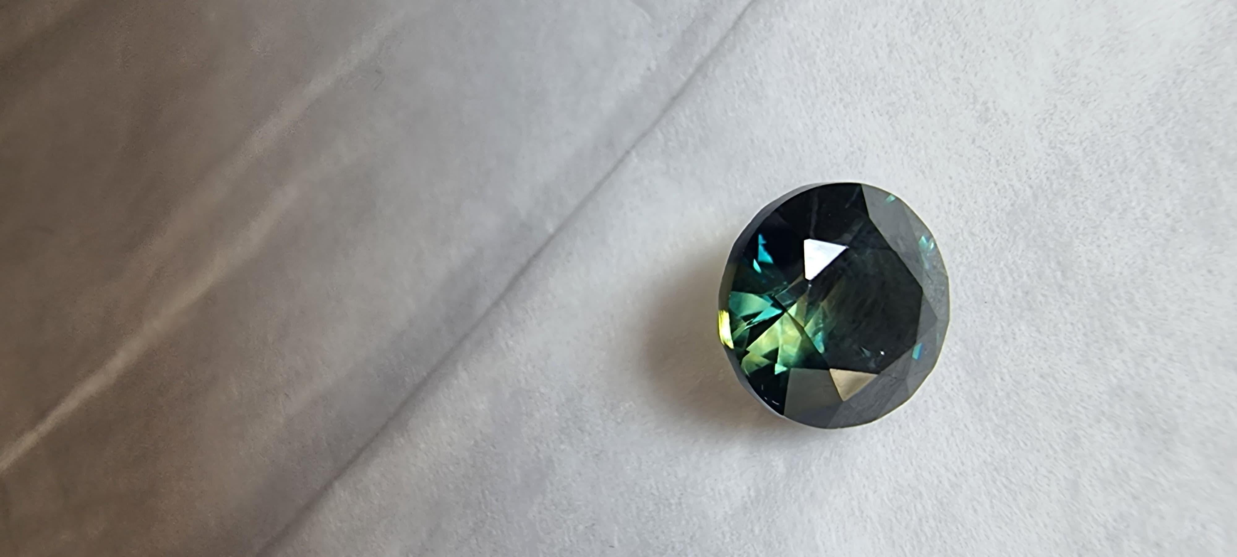 Experimenta el epítome de la belleza y el lujo auténticos con la Gema Suelta Zafiro Azul Teal Natural de Corte Brillante Redondo de 3.11 ct. Esta exquisita gema emana un profundo y seductor tono azul que cautivará a los entendidos más