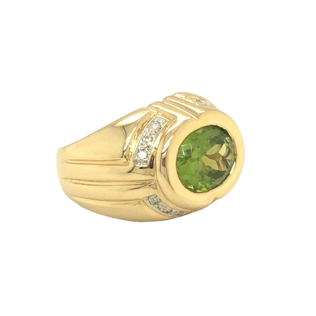 Circa 1970s this beautiful wide band ring features an oval shaped luscious green peridot weighing 3.11 carats. The bezel set is accented by small colorless diamond weighing approximately 0.15 carat total. Small cut out hearts inside the ring adds