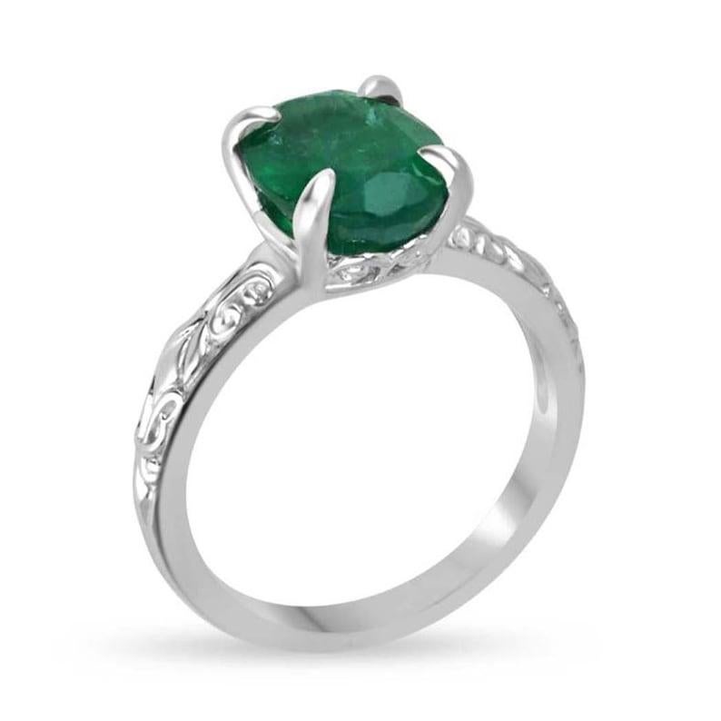 This stunning solitaire ring features a 3.11-carat Zambian emerald, glowing with a deep, rich green hue and beautifully cut in an elegant oval shape. Set securely in a four-prong setting, the emerald is complemented by a unique floral-styled shank