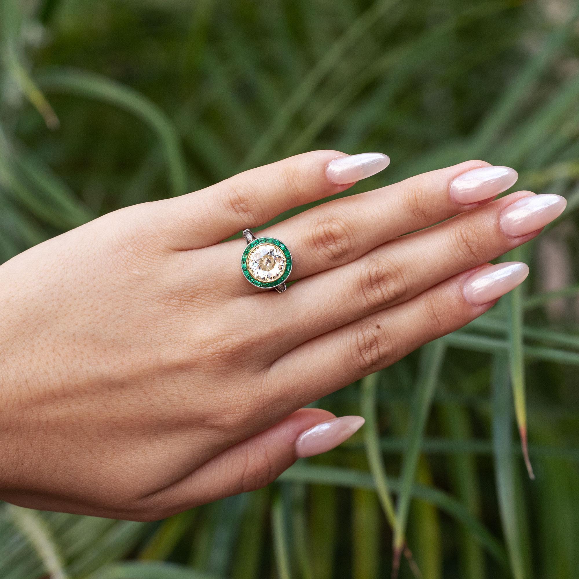 An important vintage revival, newly created from the timeless Art Deco of the 1920s. The stunning central diamond is an antique, old European cut blessed with a captivating shimmer. Encircled with a garden of Calibre cut emeralds, the entirety of