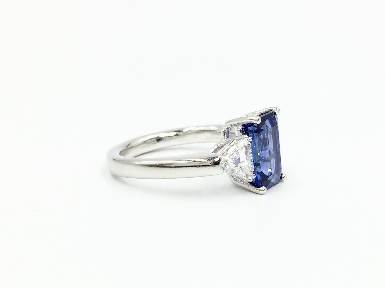 A classic blue sapphire and diamond three stone platinum ring using exceptional quality stones by high-end jewelry designer J. Stella. Center features an exquisite, highly saturated 3.13 carat emerald cut blue sapphire with the perfect amount of