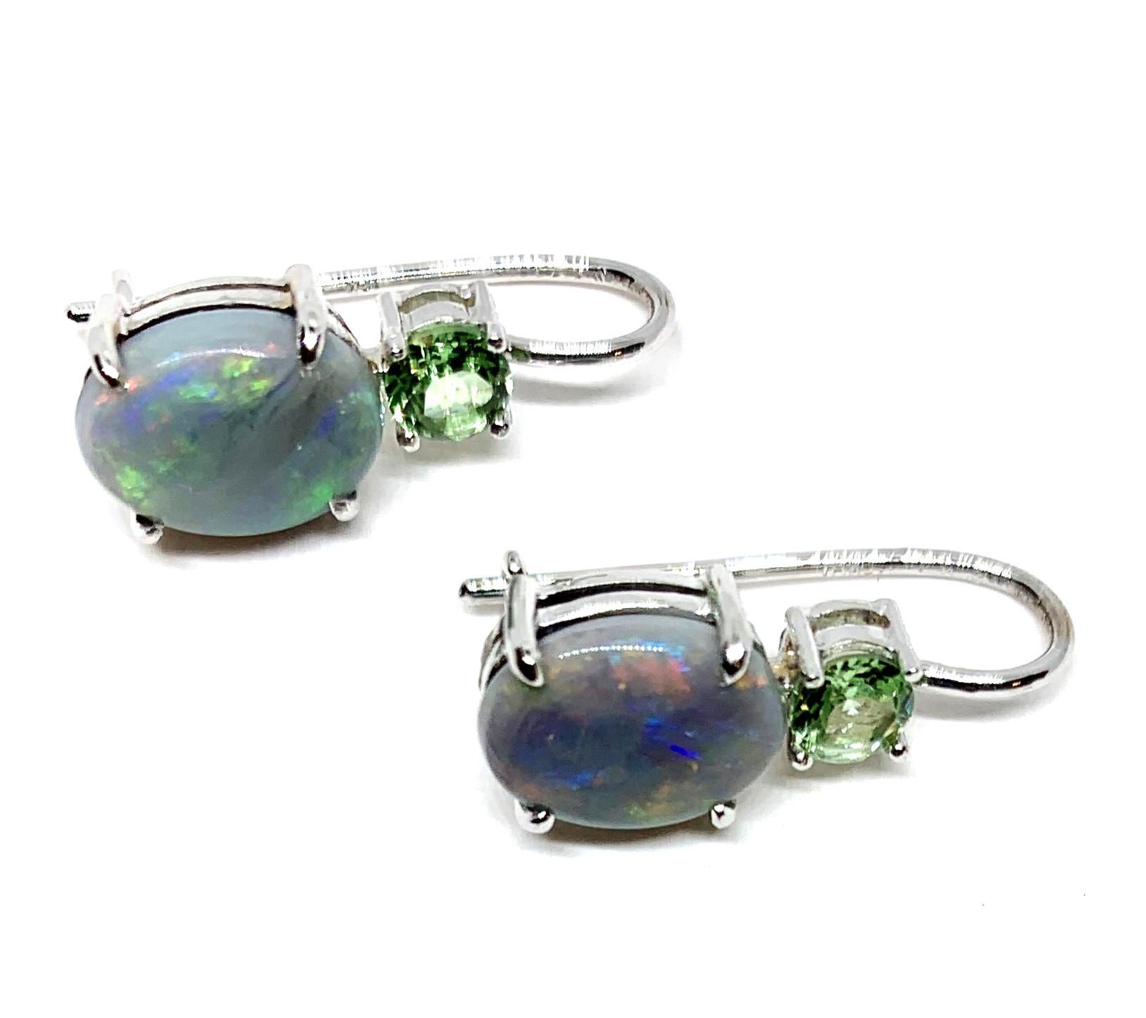 The color pairing of semi-black opals with pastel green overtones and pastel tsavorite garnets of the same color of green is both subtle and beautiful. They are cool color tones that we have set in 18k white gold handmade lever-back earrings. Oval
