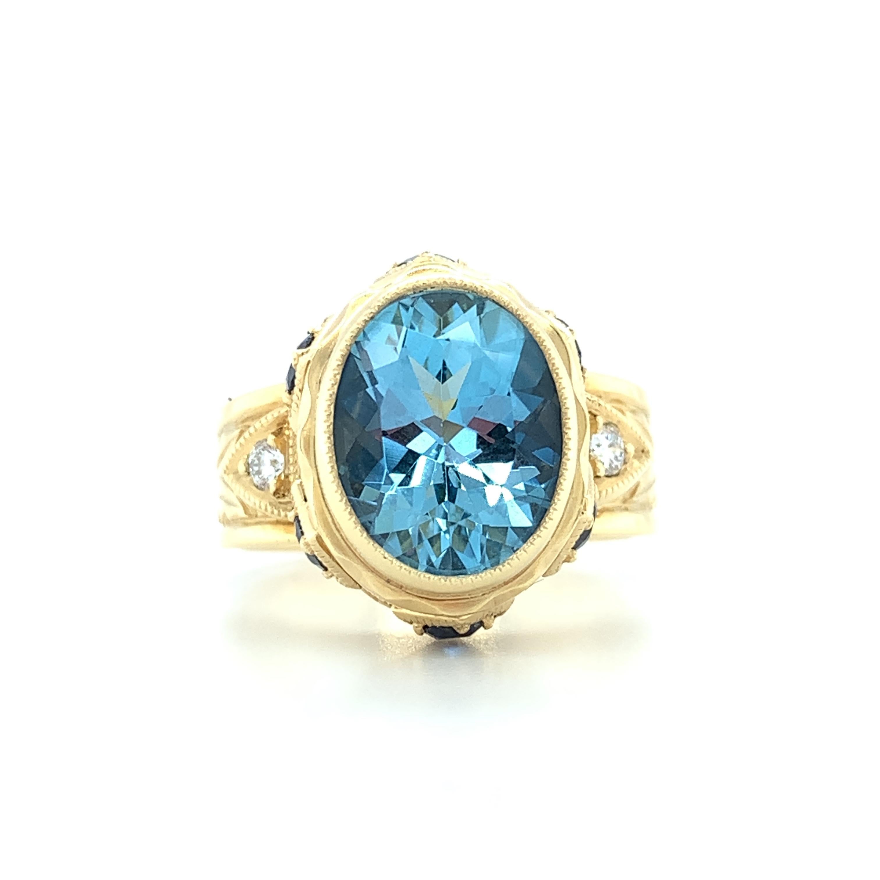 The gorgeous, crystalline aquamarine featured in this handmade 18k yellow gold ring is beautifully faceted and has strikingly rich color! The center gemstone is set in a high bezel that has been accented with royal blue sapphires and engraved by