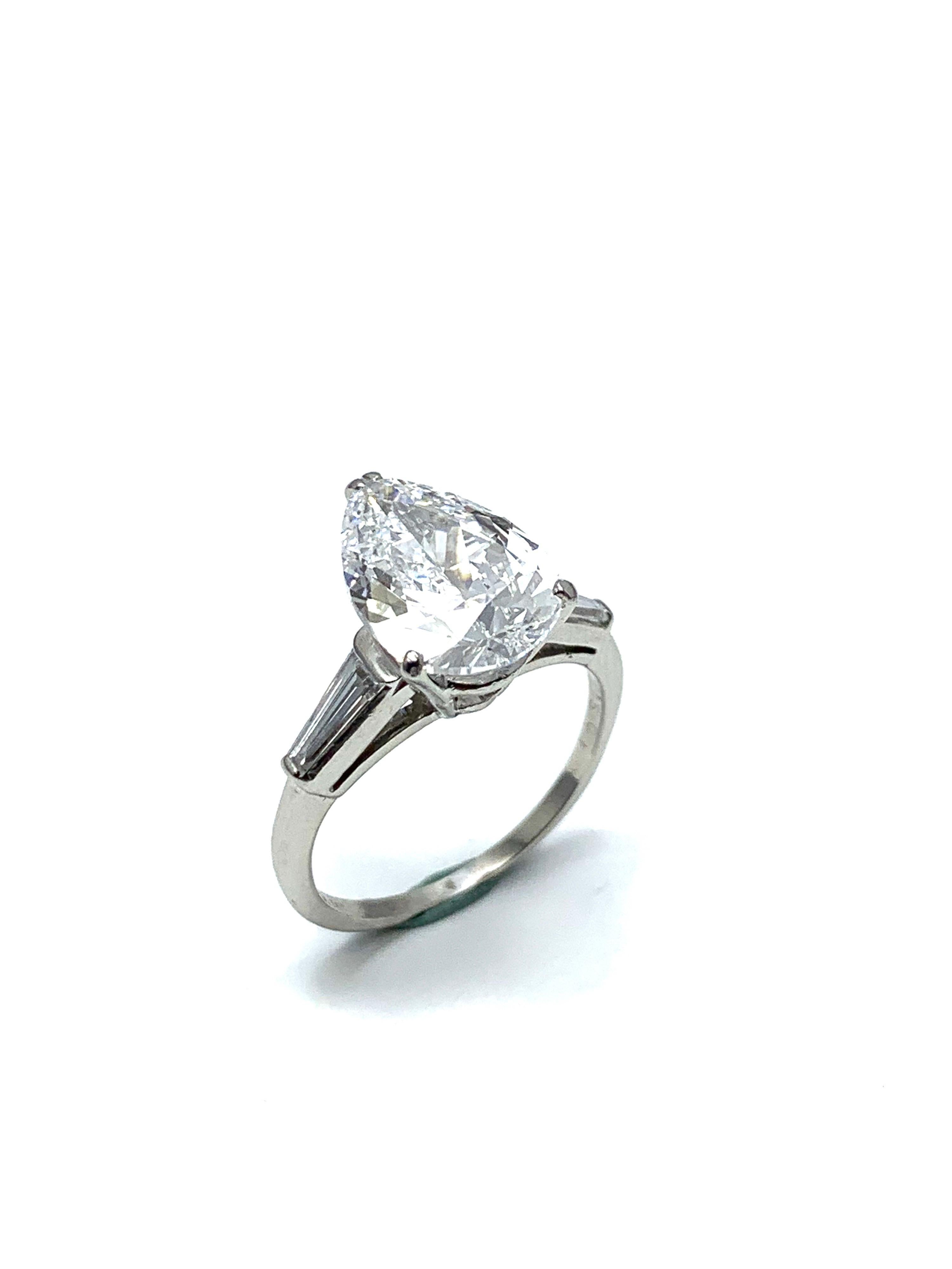An absolutely stunning 3.14 carat pear shape Diamond and platinum ring. The pear shape is set in a four prong basket setting, with a tapered baguette Diamond on each side tapering into the shank. The 3.14 carat Diamond is graded by GIA as a D color,