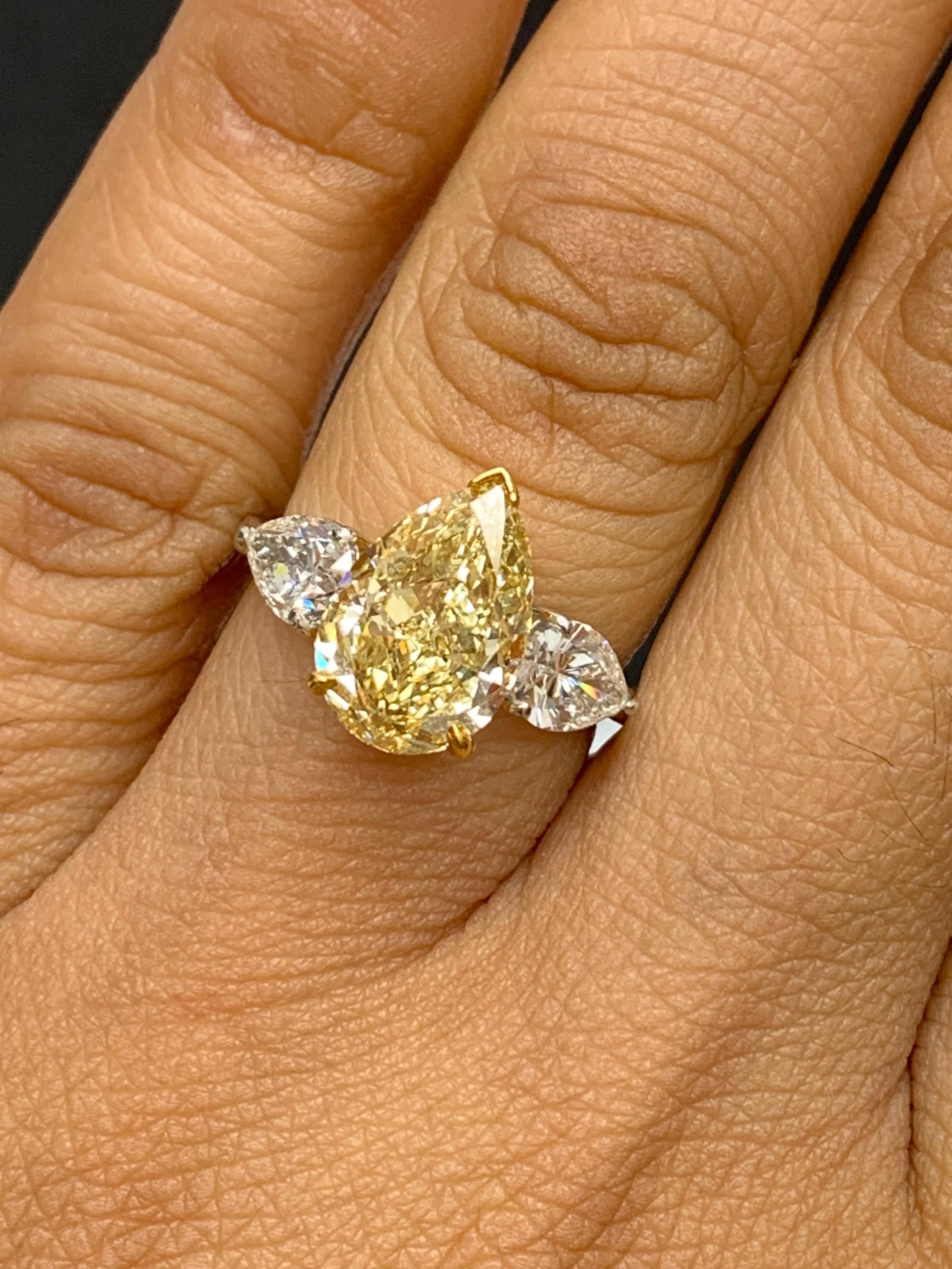 A stunning ring showcasing a rich intense pear-shaped fancy yellow diamond weighing 3.15 carats  Flanking the center stone are two brilliant pear shape diamonds, weighing 1.58 carats total, Made in platinum.