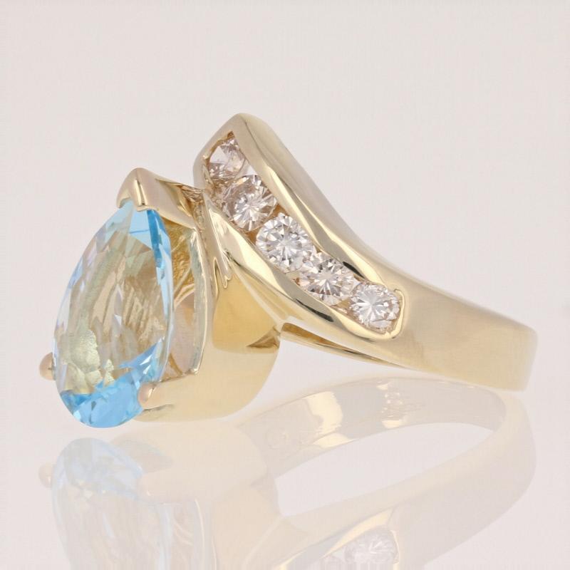 Surprise your March birthday girl with an exquisite gift she will always treasure! Featuring a dazzling bypass style, this 14k yellow gold ring showcases a sparkling pear cut aquamarine solitaire set above two glittering rows of white diamonds. 