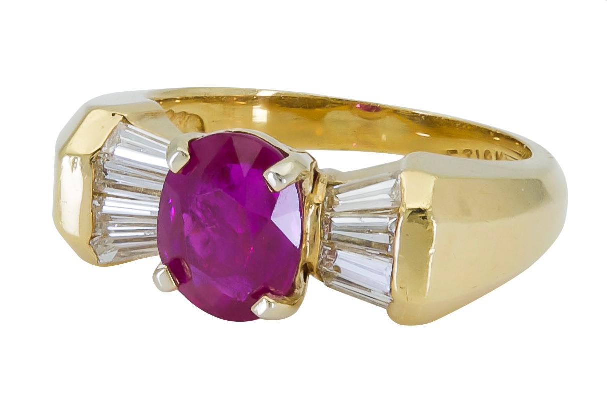 A unique and modern design showcasing a vibrant emerald cut ruby, set in a ribbon style mounting. This is achieved by flanking the center stone with inverted tapered baguette diamonds, set in an angular mounting made in 18k yellow gold. 
Ruby weighs